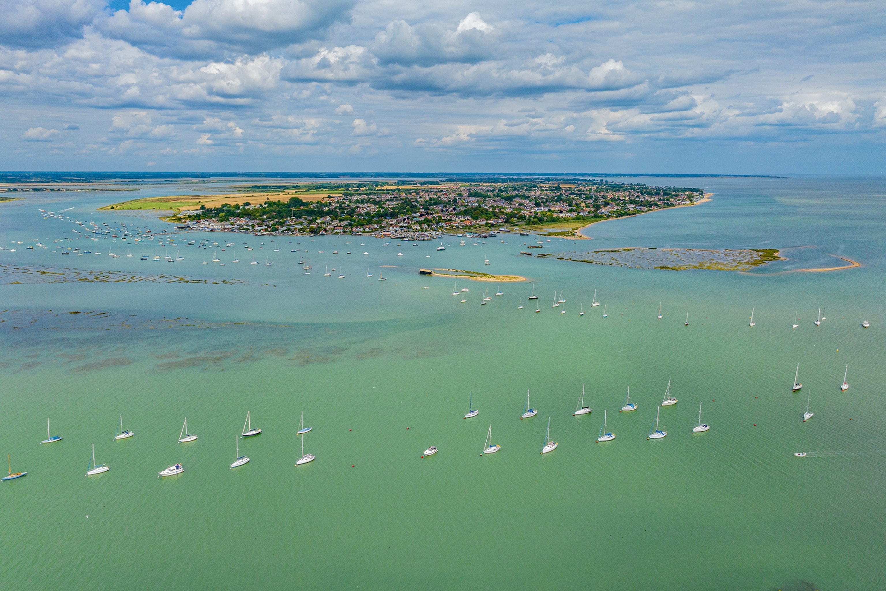 A birds-eye perspective on a small, flat island with sailing boats creating a halo in the surrounding waters.