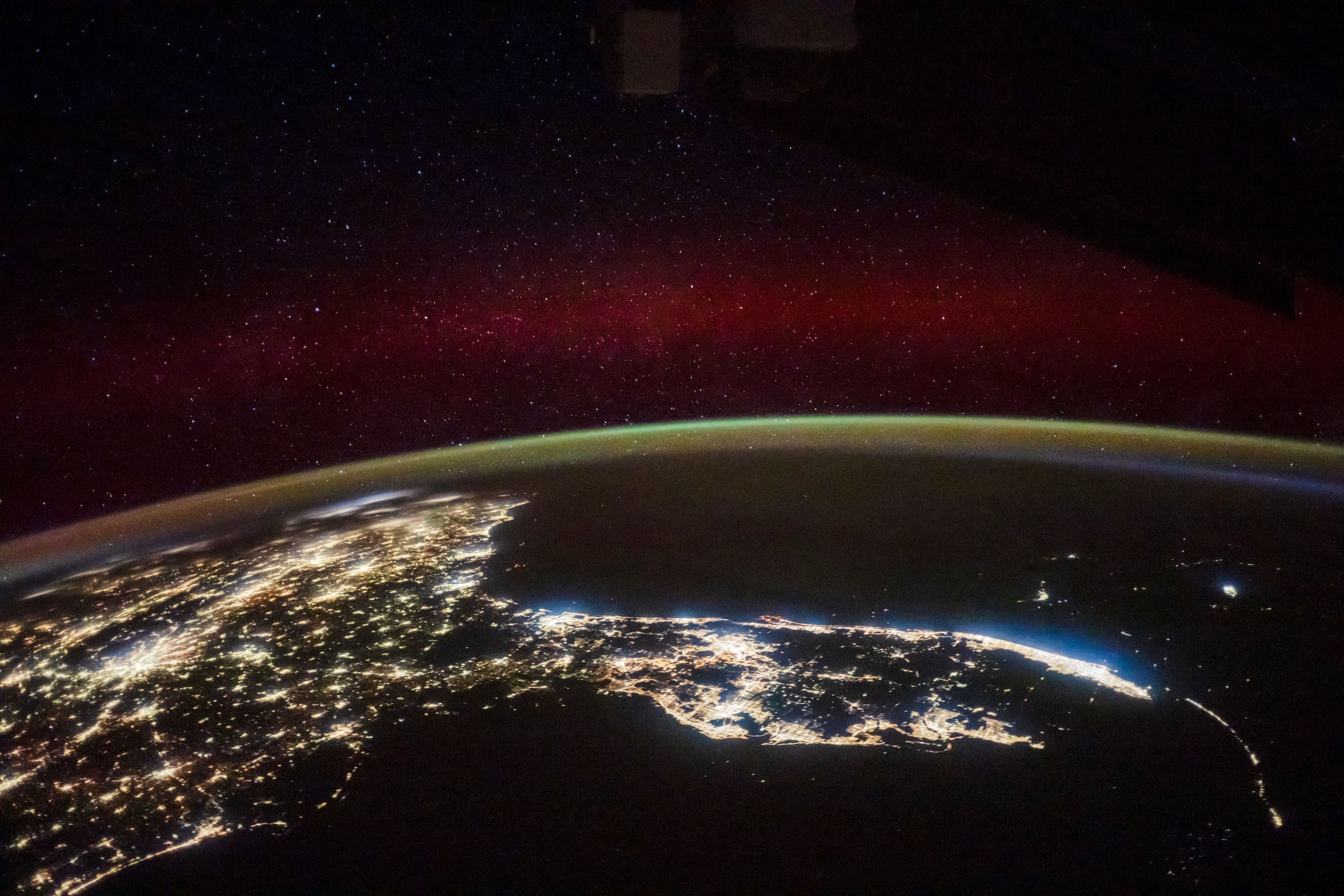 A photo of the earth from outer space with bright lights all over the globe and a slight red aurora on the horizon.