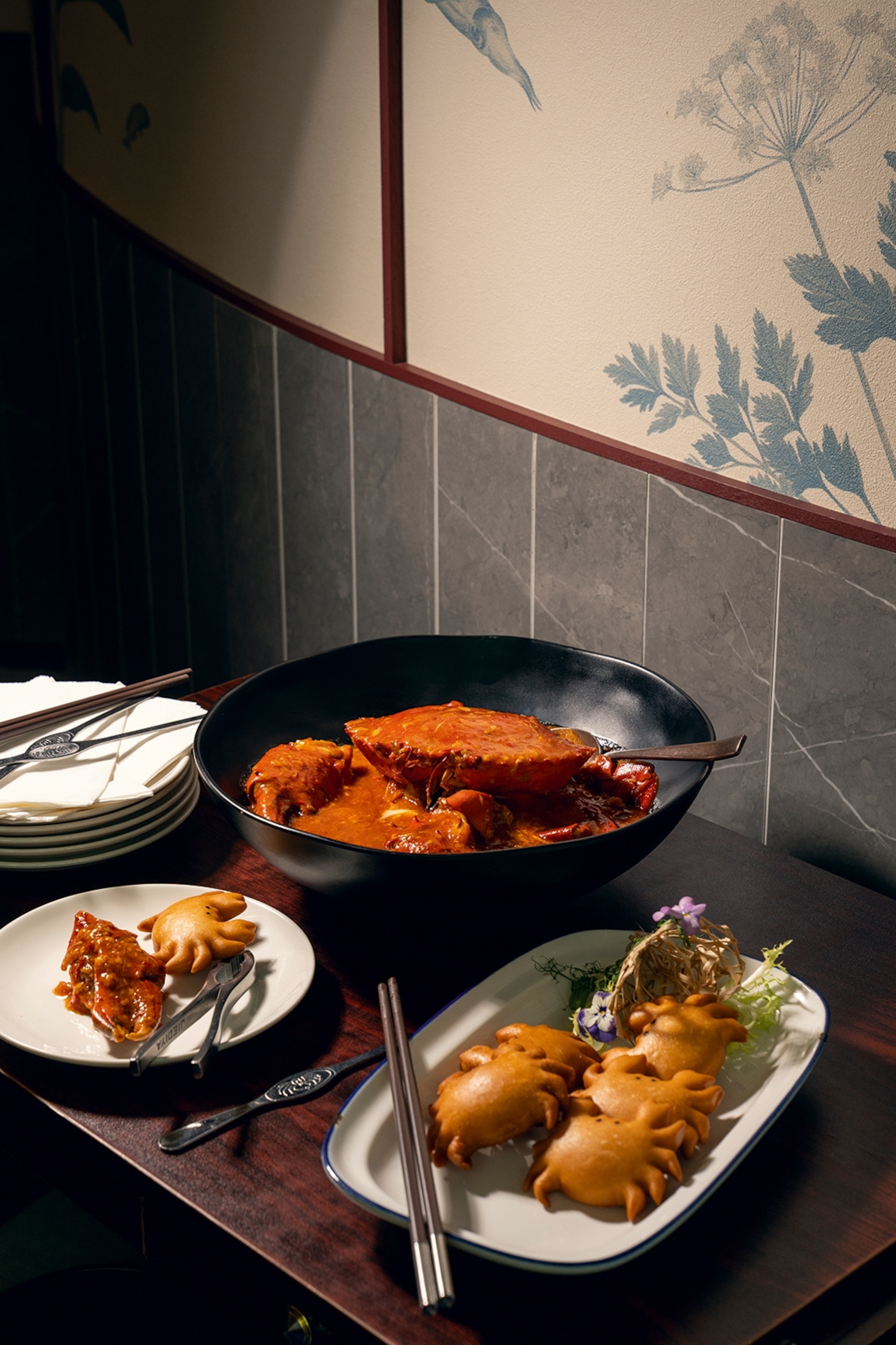 A table set with a whole chilli crab in a bowl alongside small crab-shaped buns.