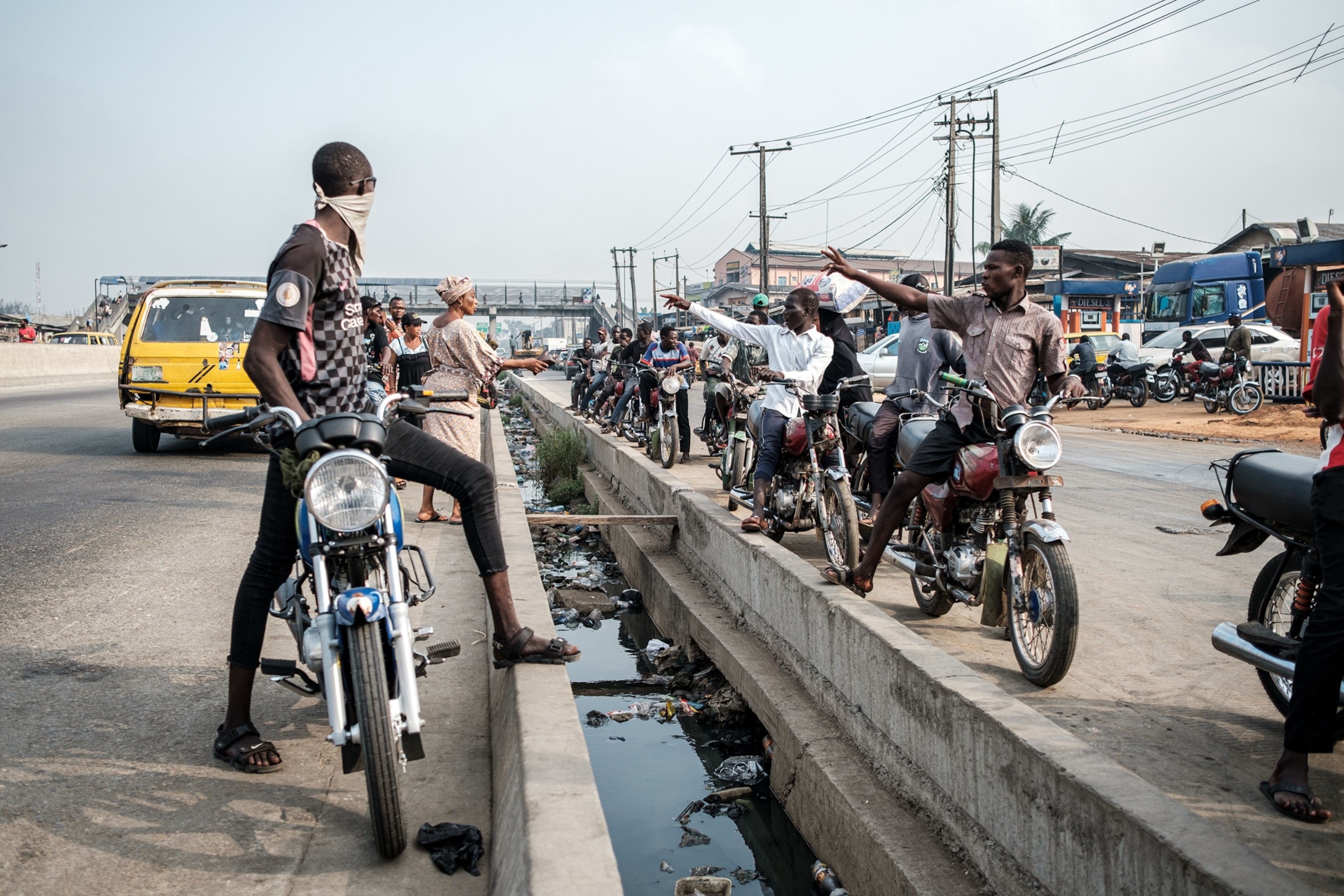 Riders picking up passengers by the traffic divider barrier with gutter in it.