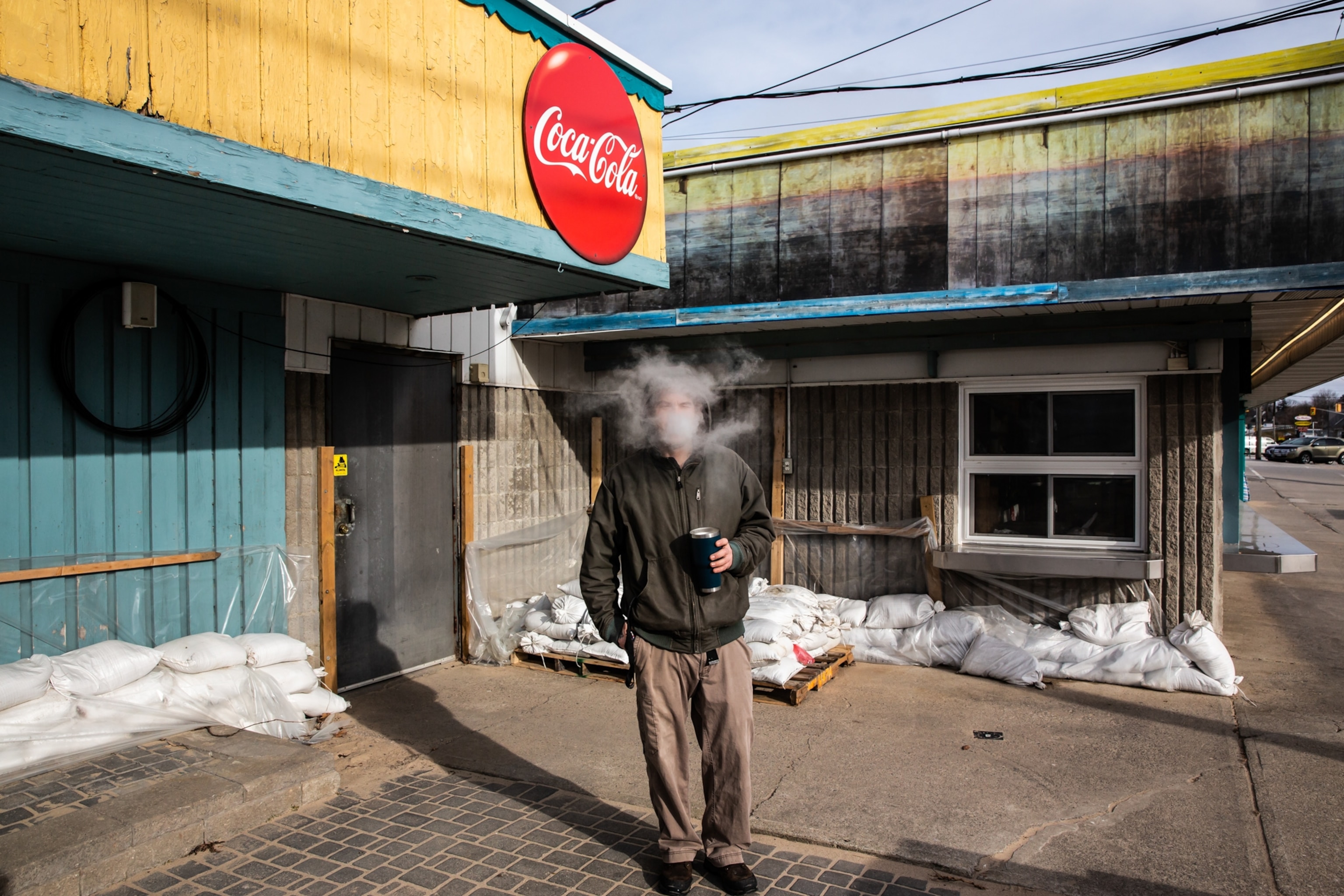 a man smoking in front of a yellow and teal store front with a coca-cola sign