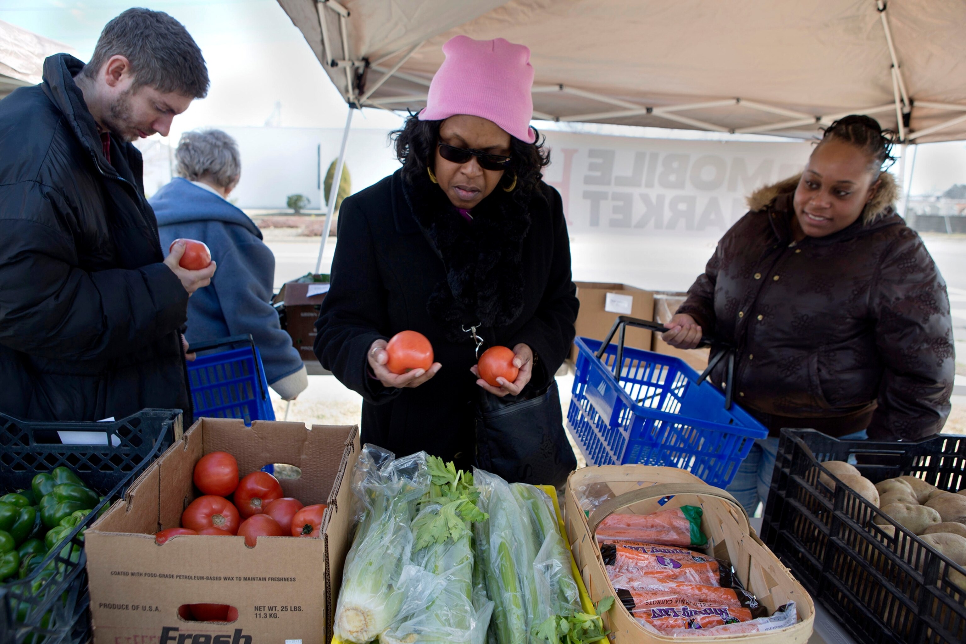 Damon Miller, left, Lana Taylor, center, and Kimberly Trower check out the fresh tomatoes at the mobile Five Points Community Farm Market behind Trinity Word of Faith Baptist Church on Ballentine Blvd in Norfolk, Va. Saturday morning, Feb. 2, 2013.