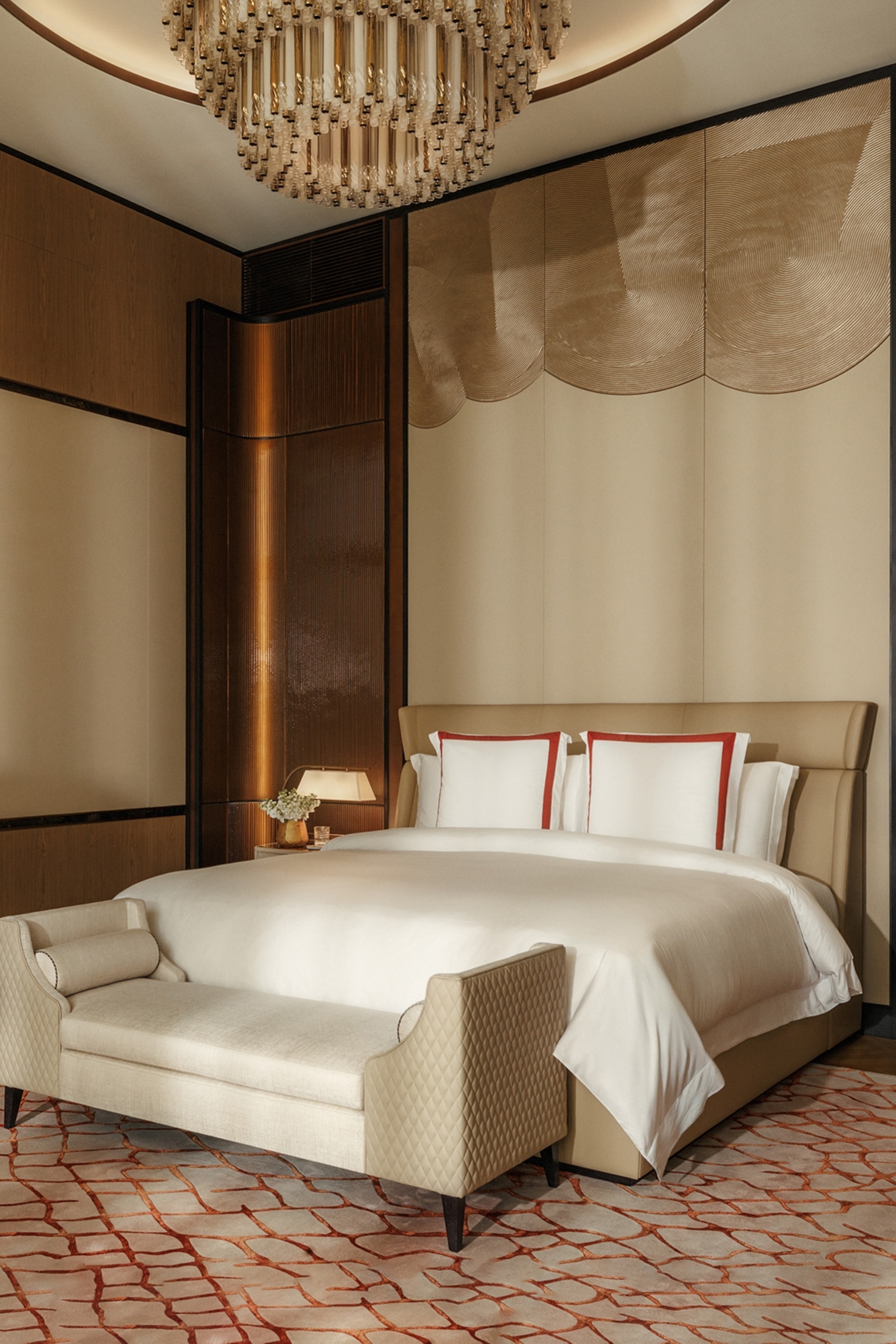 The clean yet luxurious interiors of a tall and spacious double room with a chandelier hung above the bed and tasteful wall panelling behind.