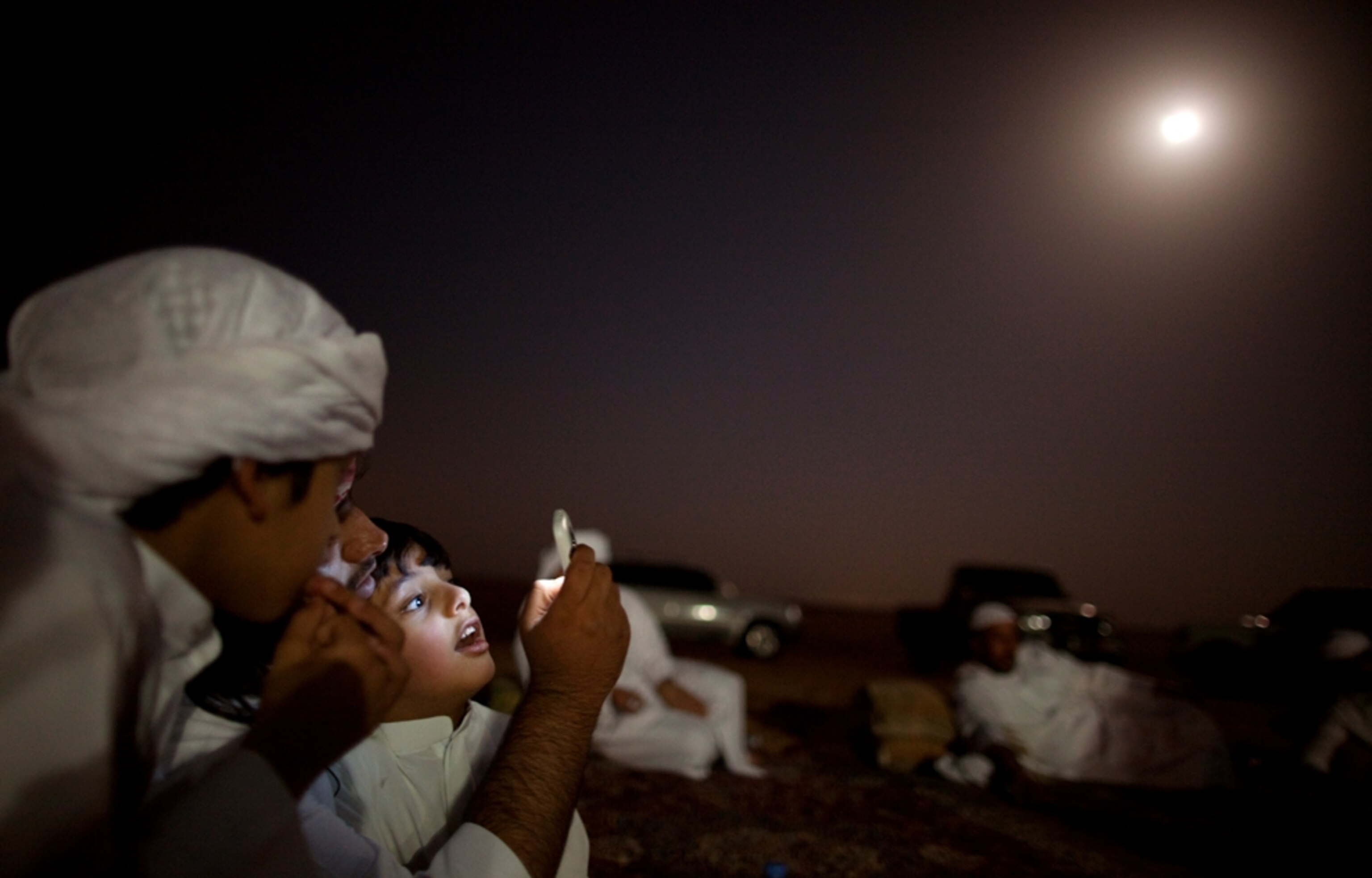 A young boy looks at a cell phone at night in the desert