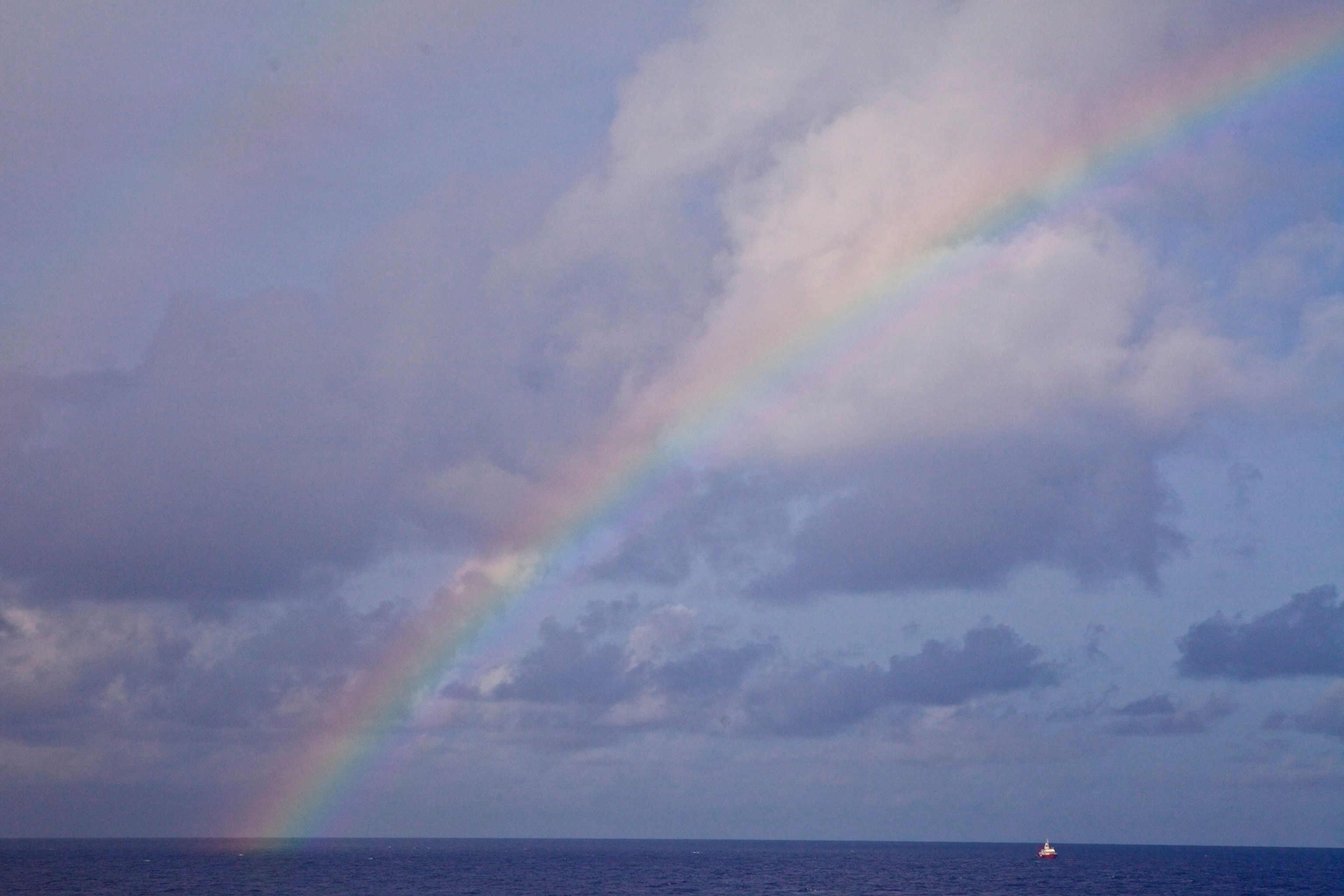 A rainbow arcs over the open ocean on a cloudy day