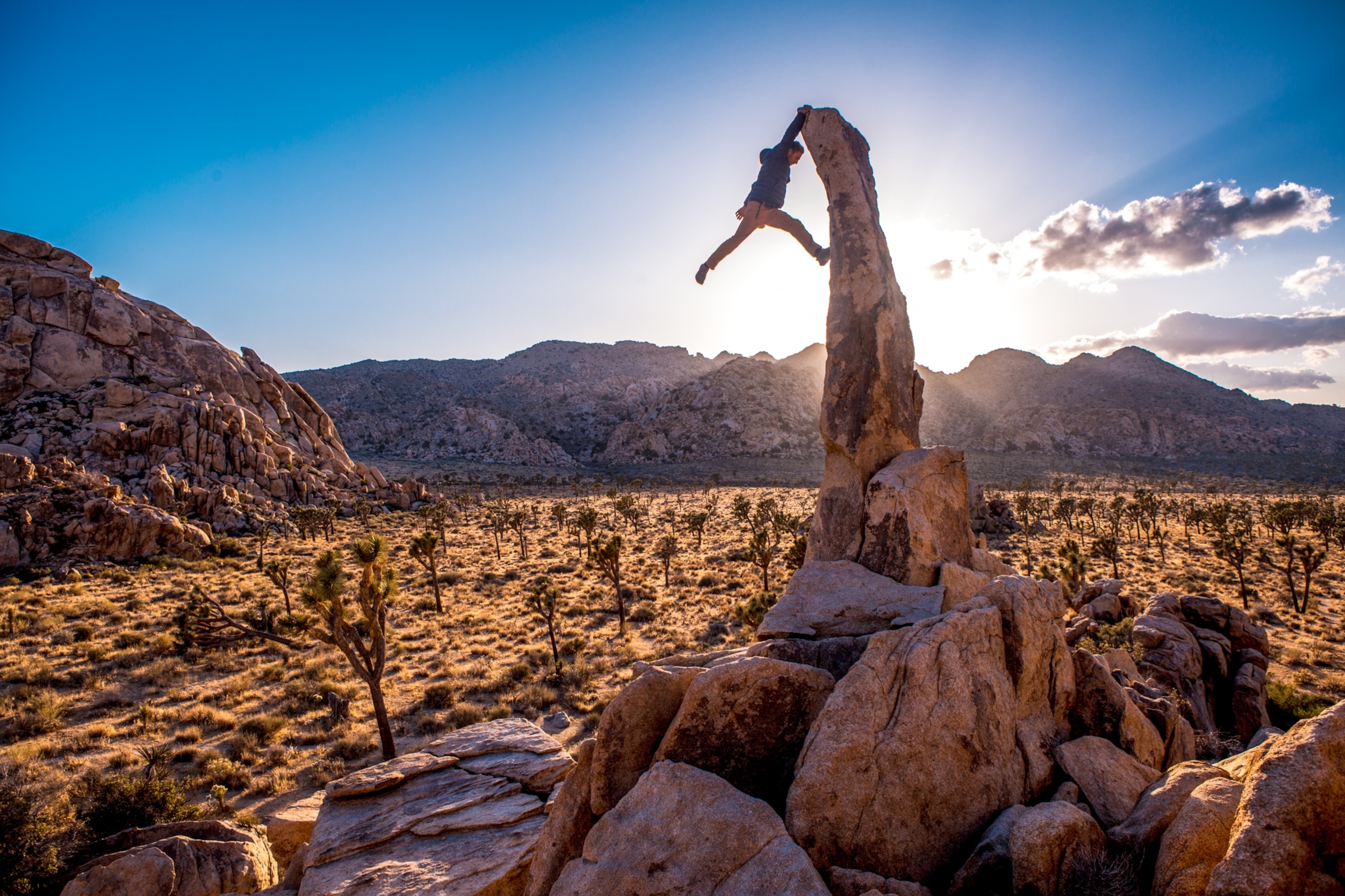 A climber silhouetted as they hang from the peak of a pointy bouldering route in the desert