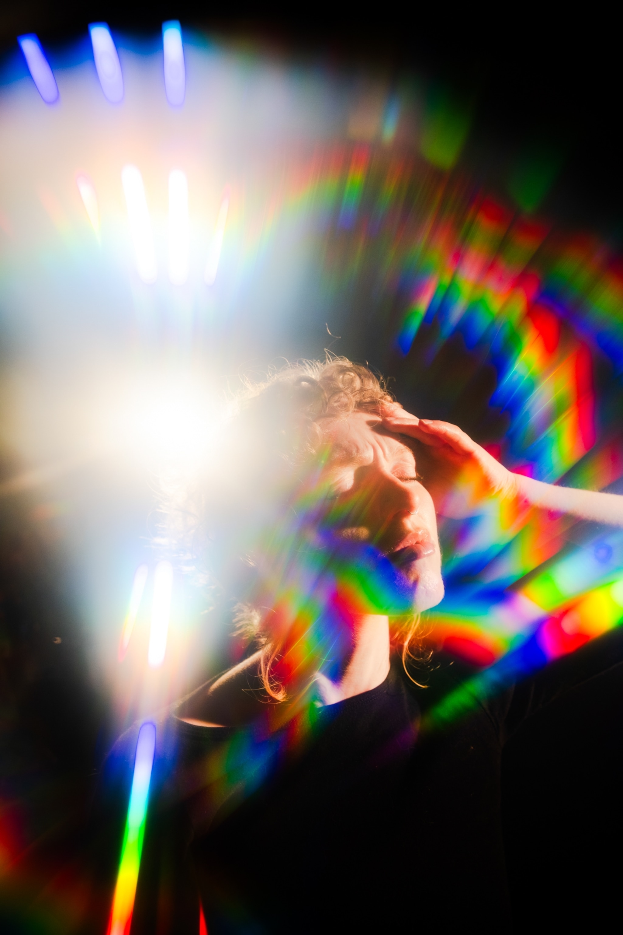 A woman clutching her temples in pain as bright colorful lights shine around her