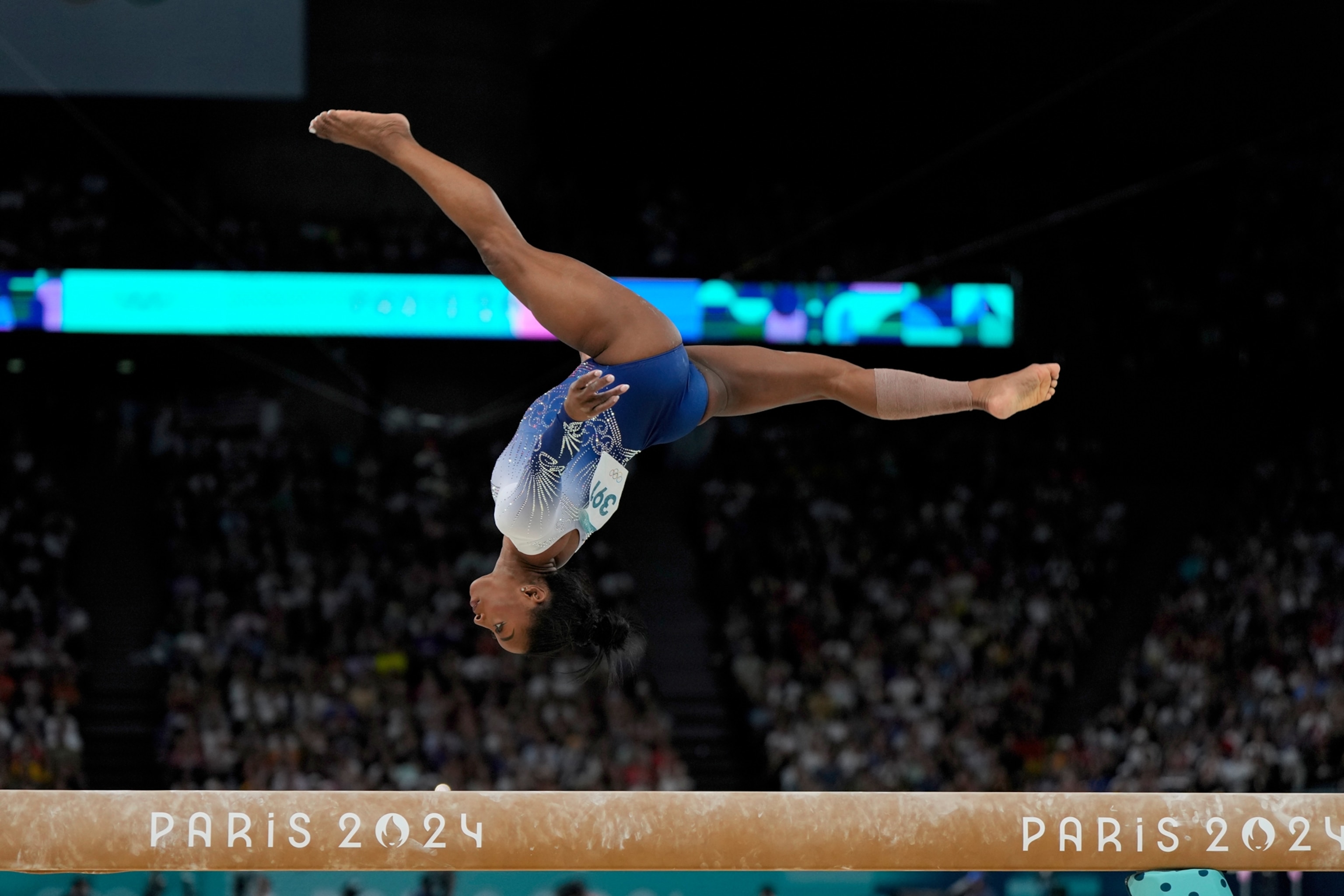 A woman does a back flip over a balance beam