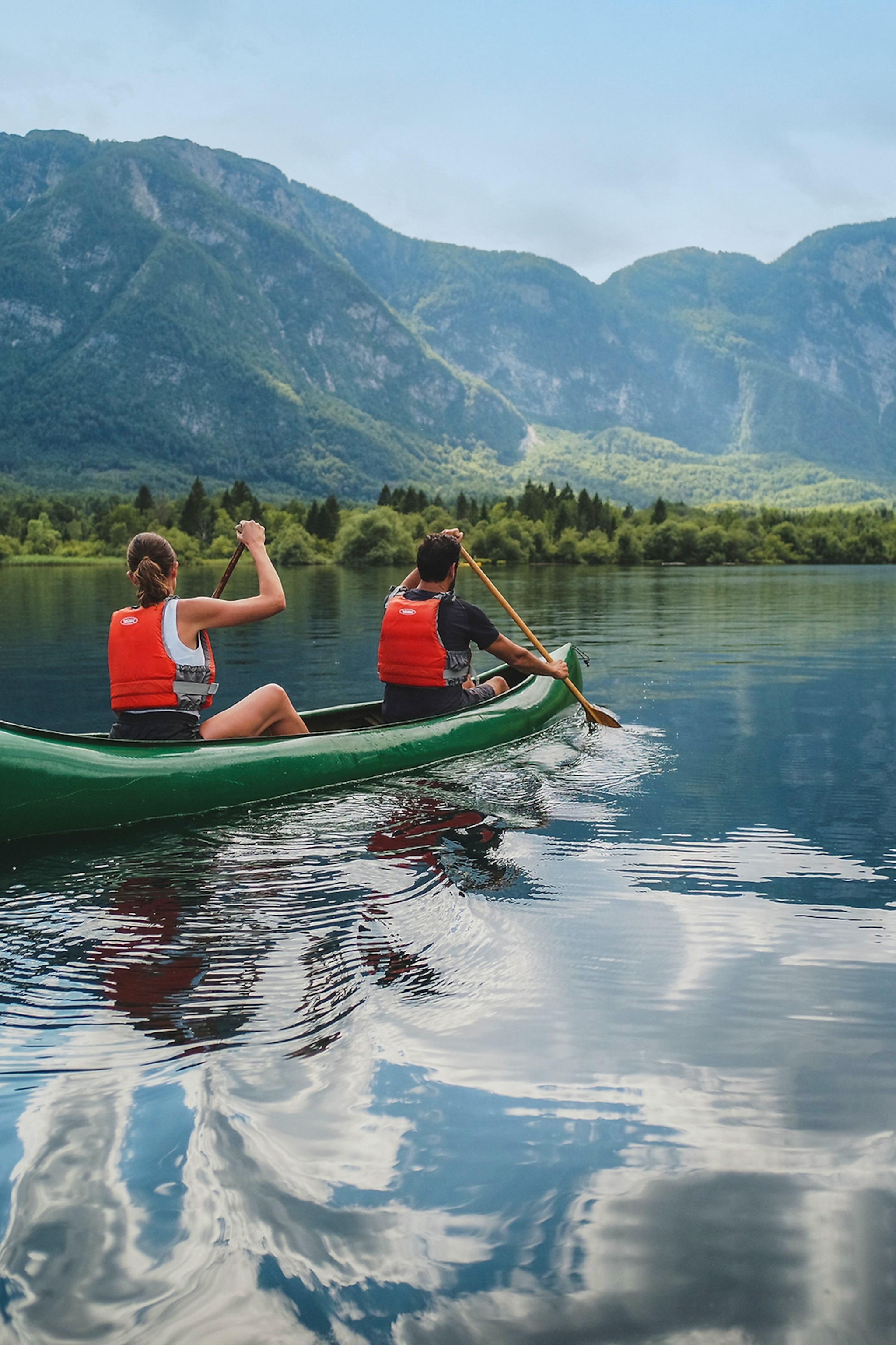 A couple in a canoe rowing down a lake with mountains in the background.