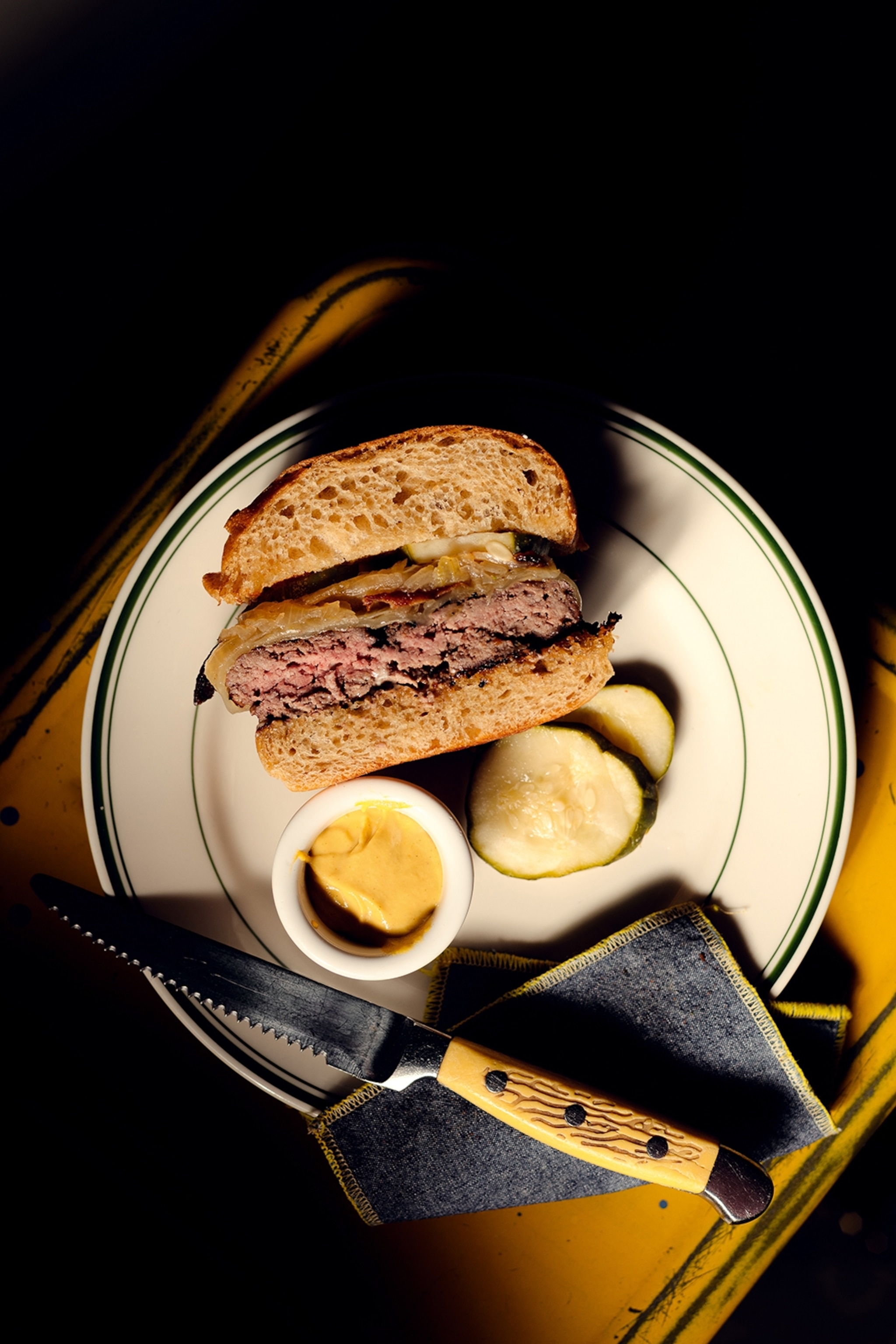 A plate with half a burger, pickles and mustard.