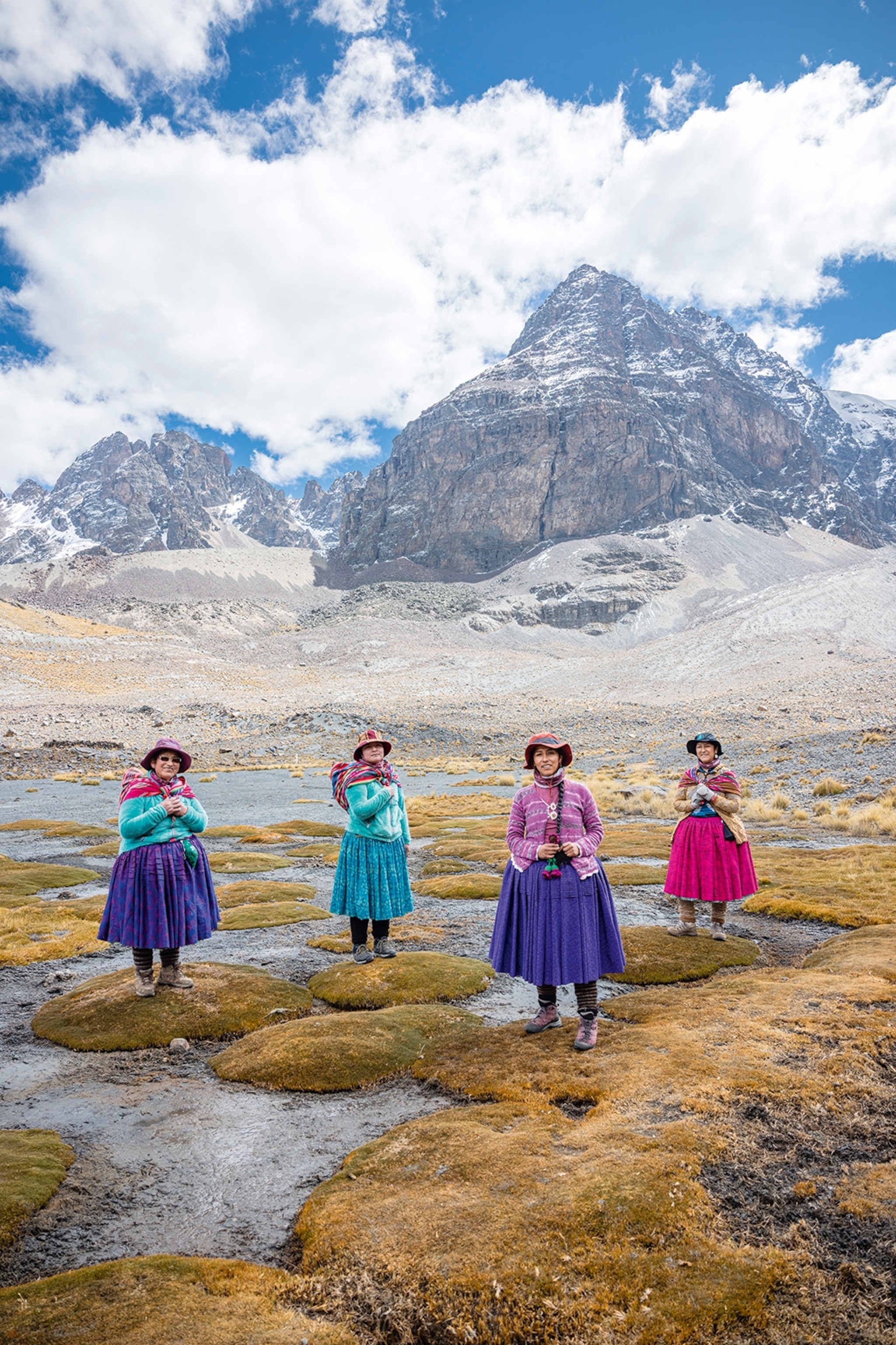 Four women in traditionally puffy skirts and hiking gear posing on a mountian plateau.