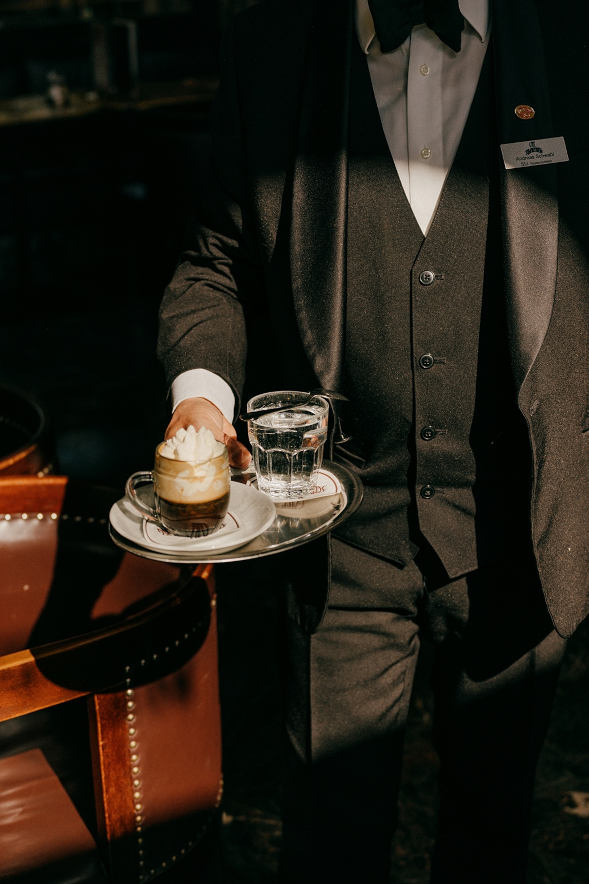 A sun spotlight on a waiter holding a silver tray of coffee with whipped cream and a glass of water.