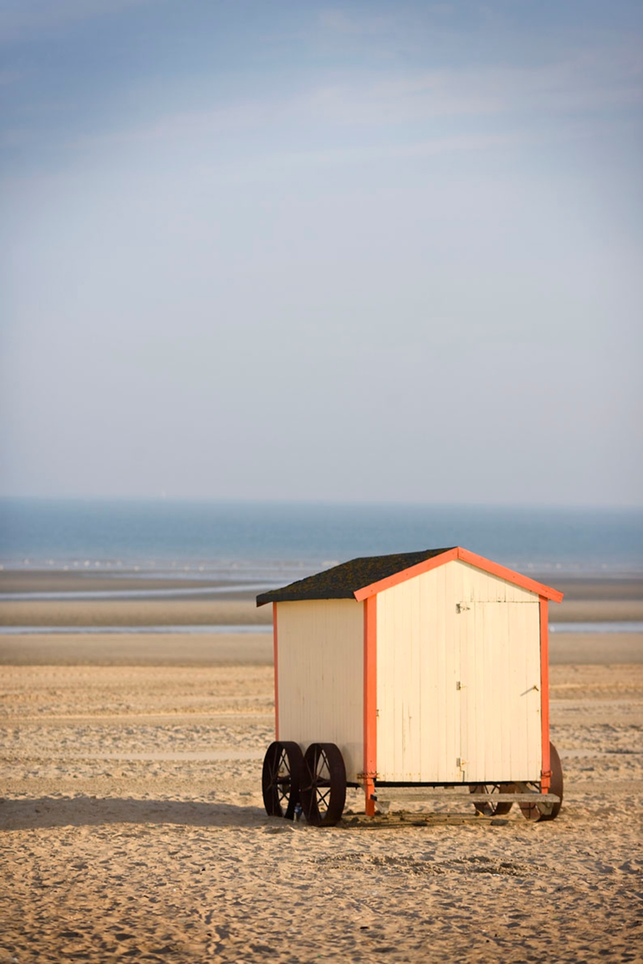 A bathing hut with wheels on the beach with sea in background.