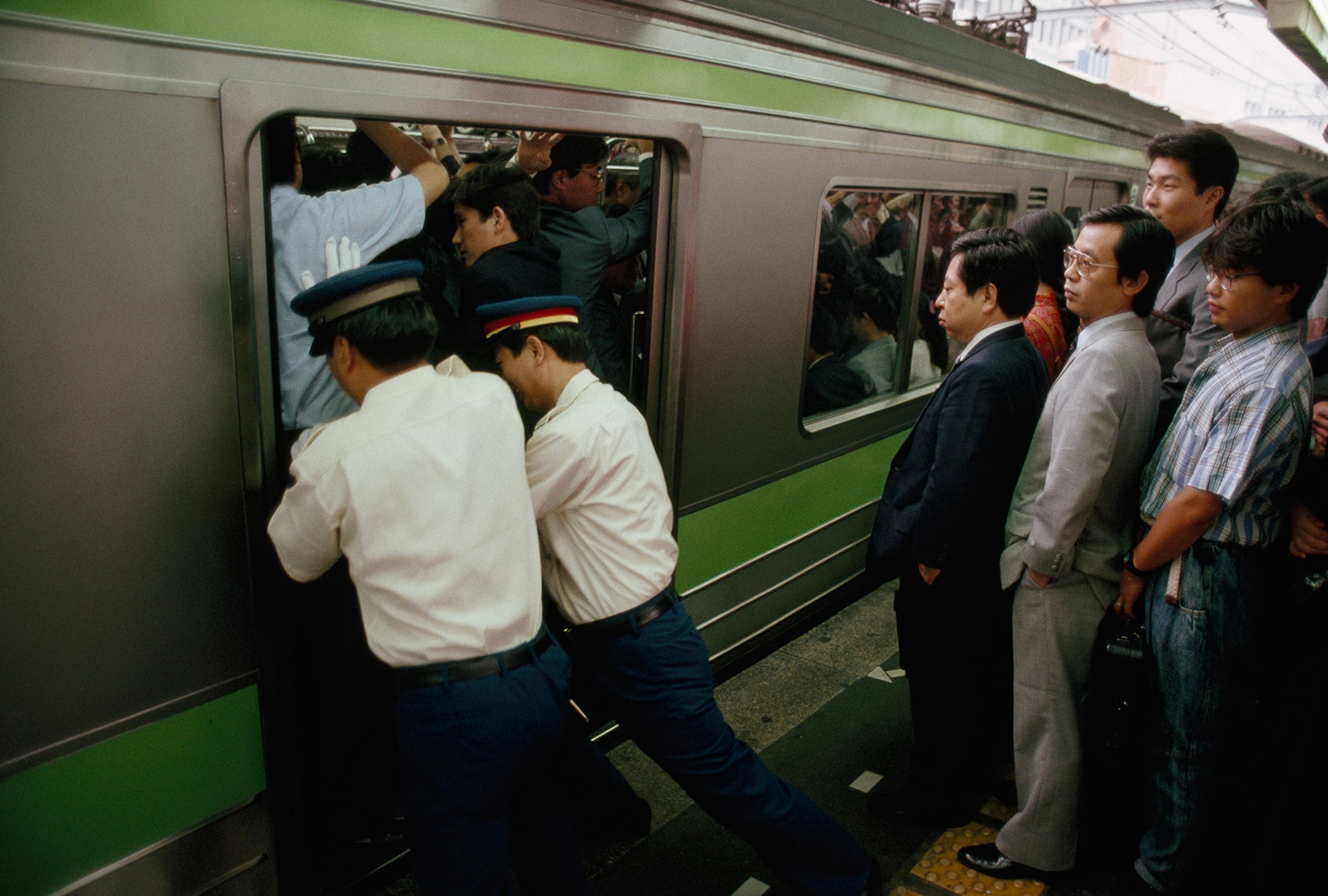 Japanese rail station attendants pushing commuters on to trains