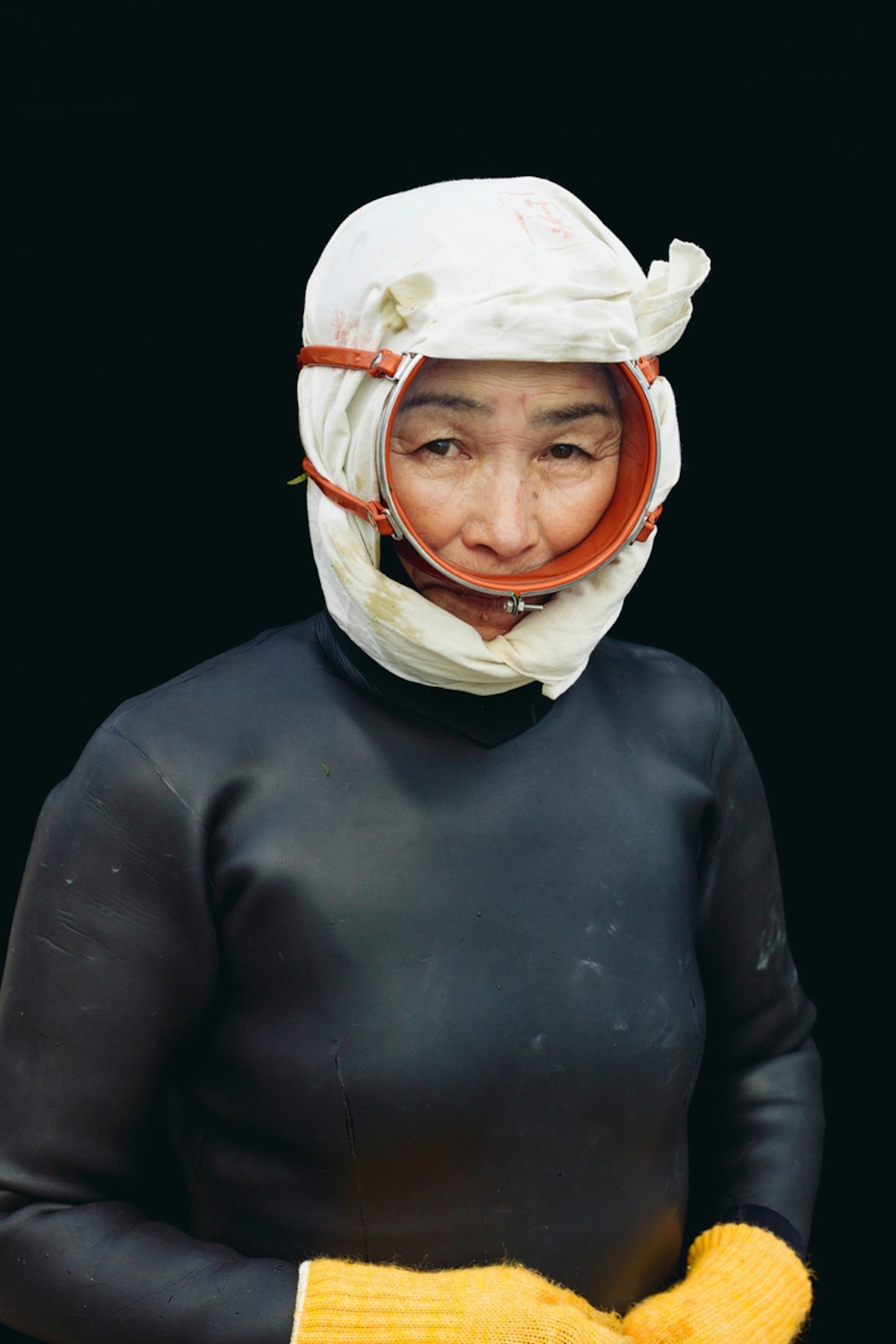 A portrait of an elderly, female diver from Japan wearing round full-face goggles and a wet suit.