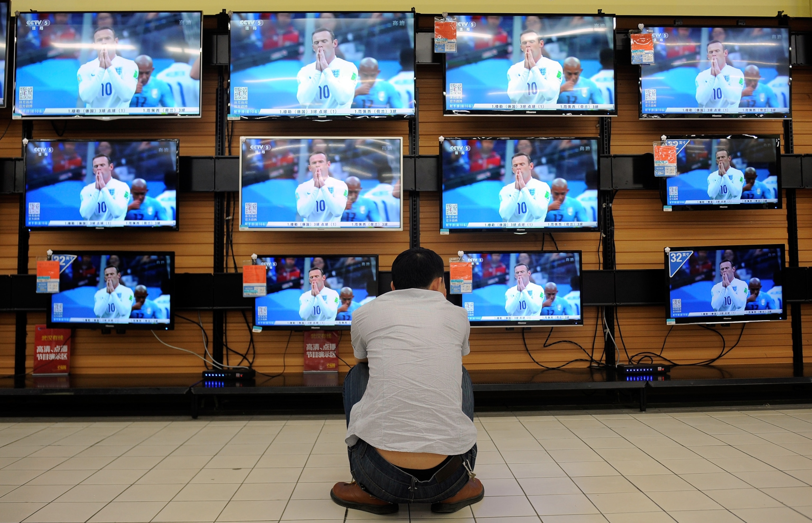 A man crouches in front of television sets broadcasting recorded footage of 2014 Brazil World Cup group D match between England and Uruguay.