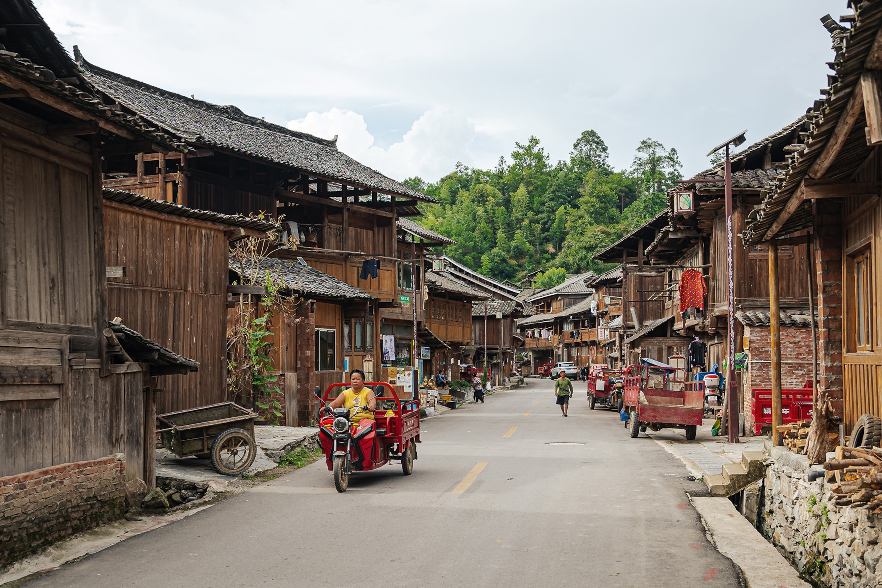 A busy village street lined with simple, wooden houses and mountains in the background.