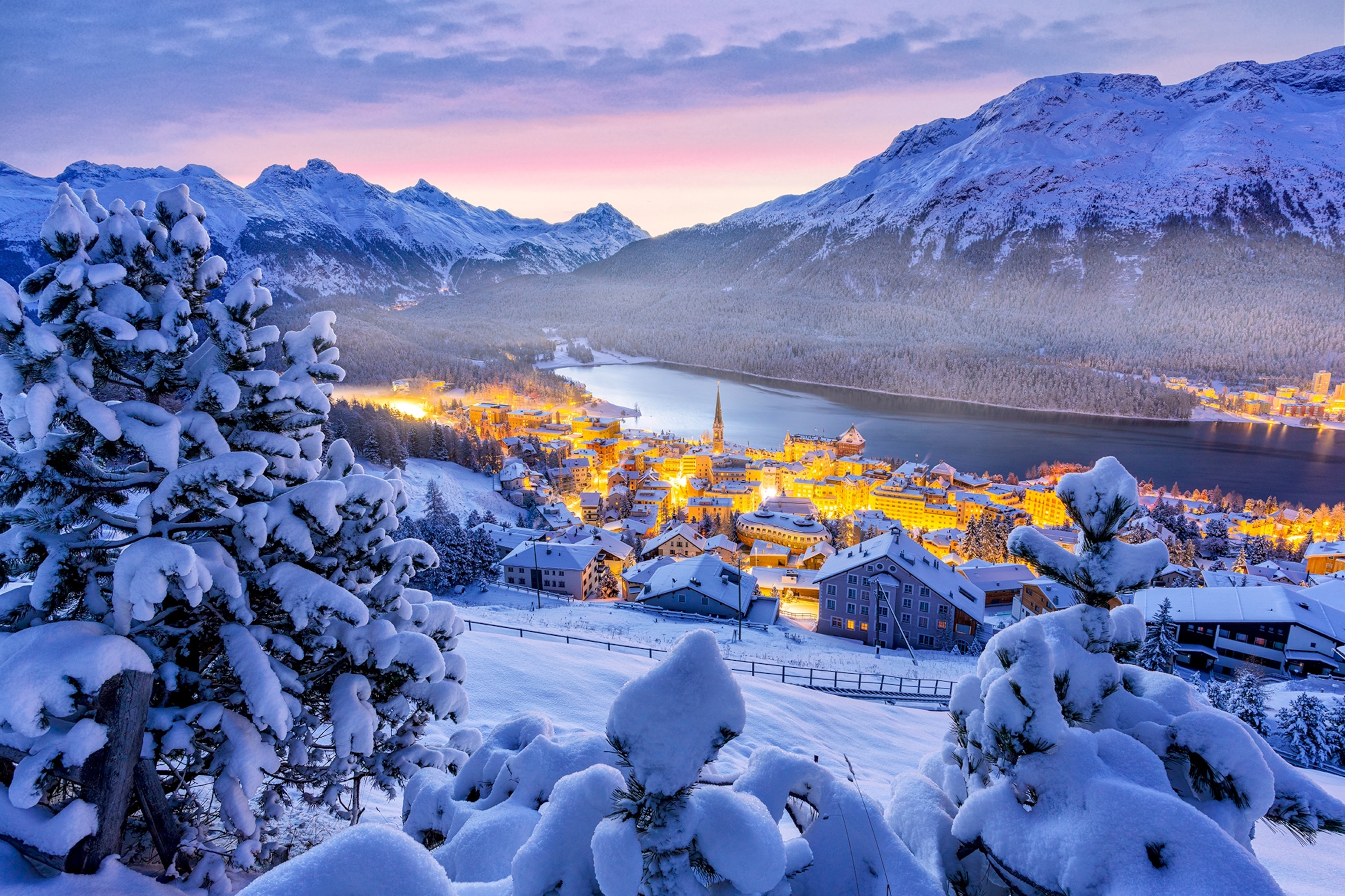 Illuminated alpine village of St. Moritz in winter snow at dusk in Switzerland