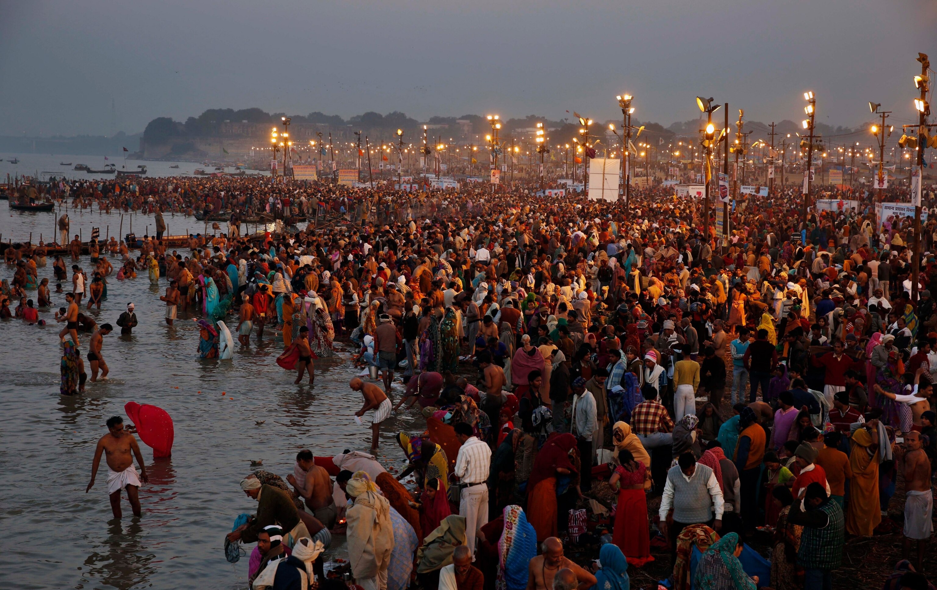A large crowd gathering by a river, some praying inside the river