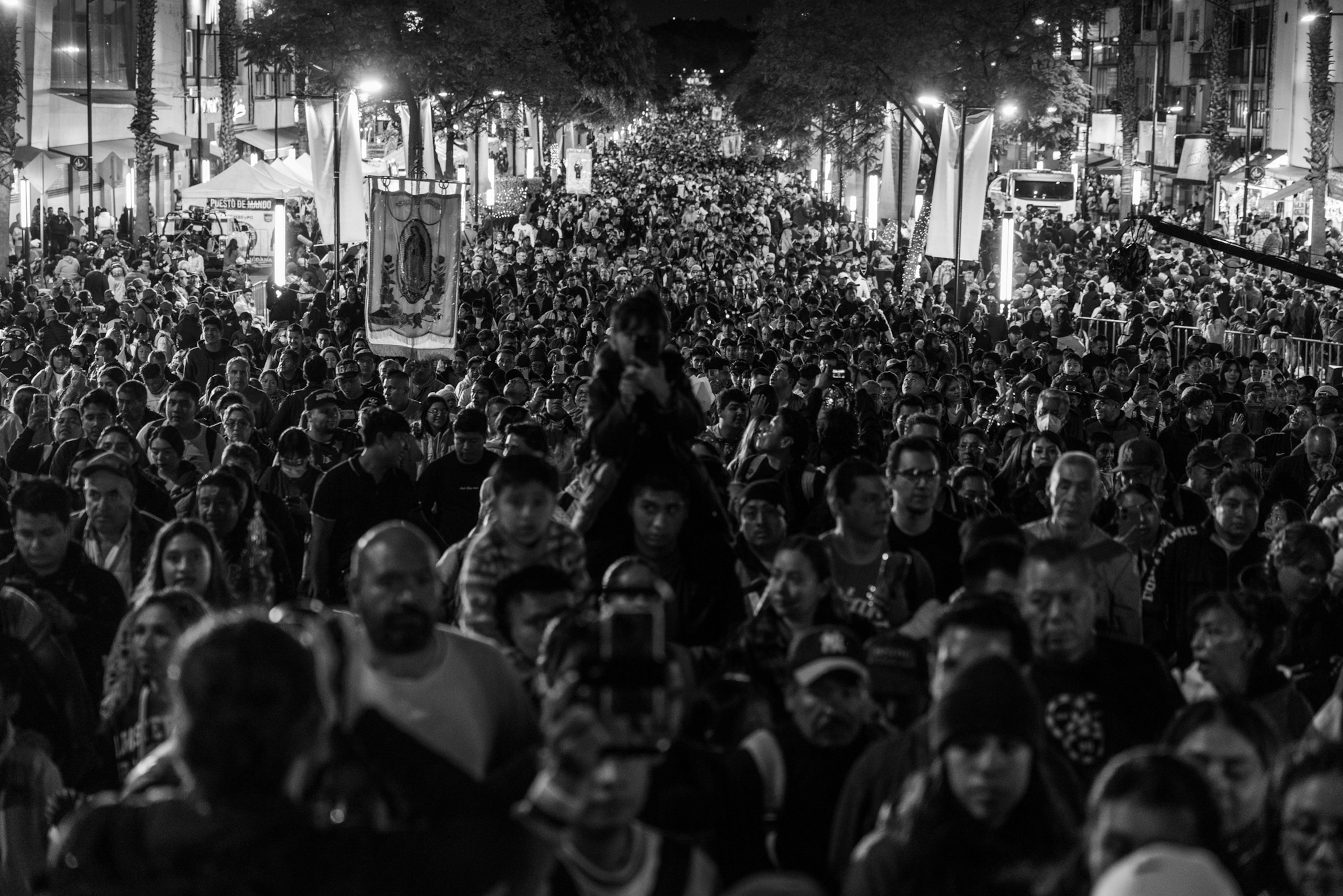 A busy crowd walks on a road with signs and lights
