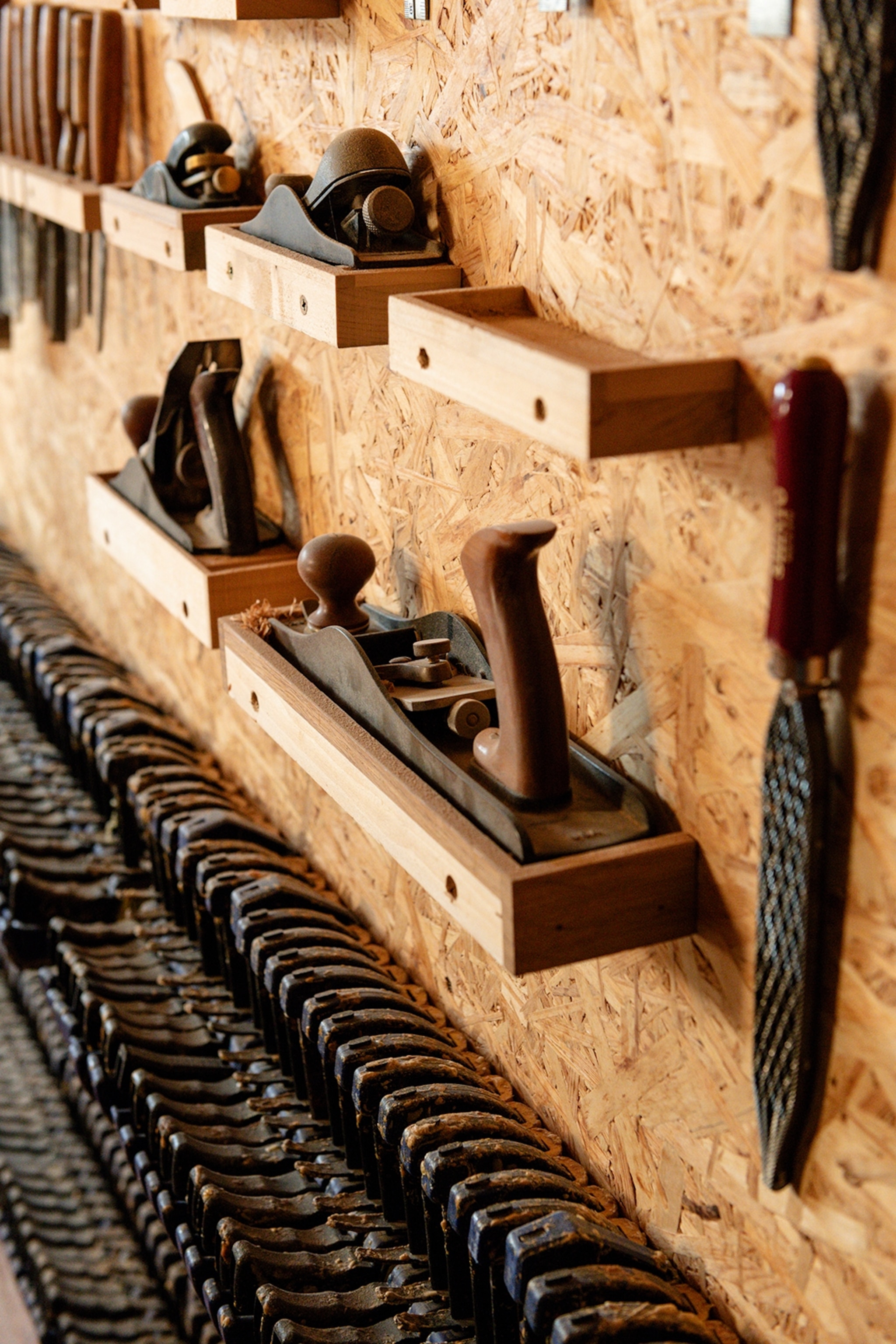 Wood carving tools lined up on a plywood shelf.