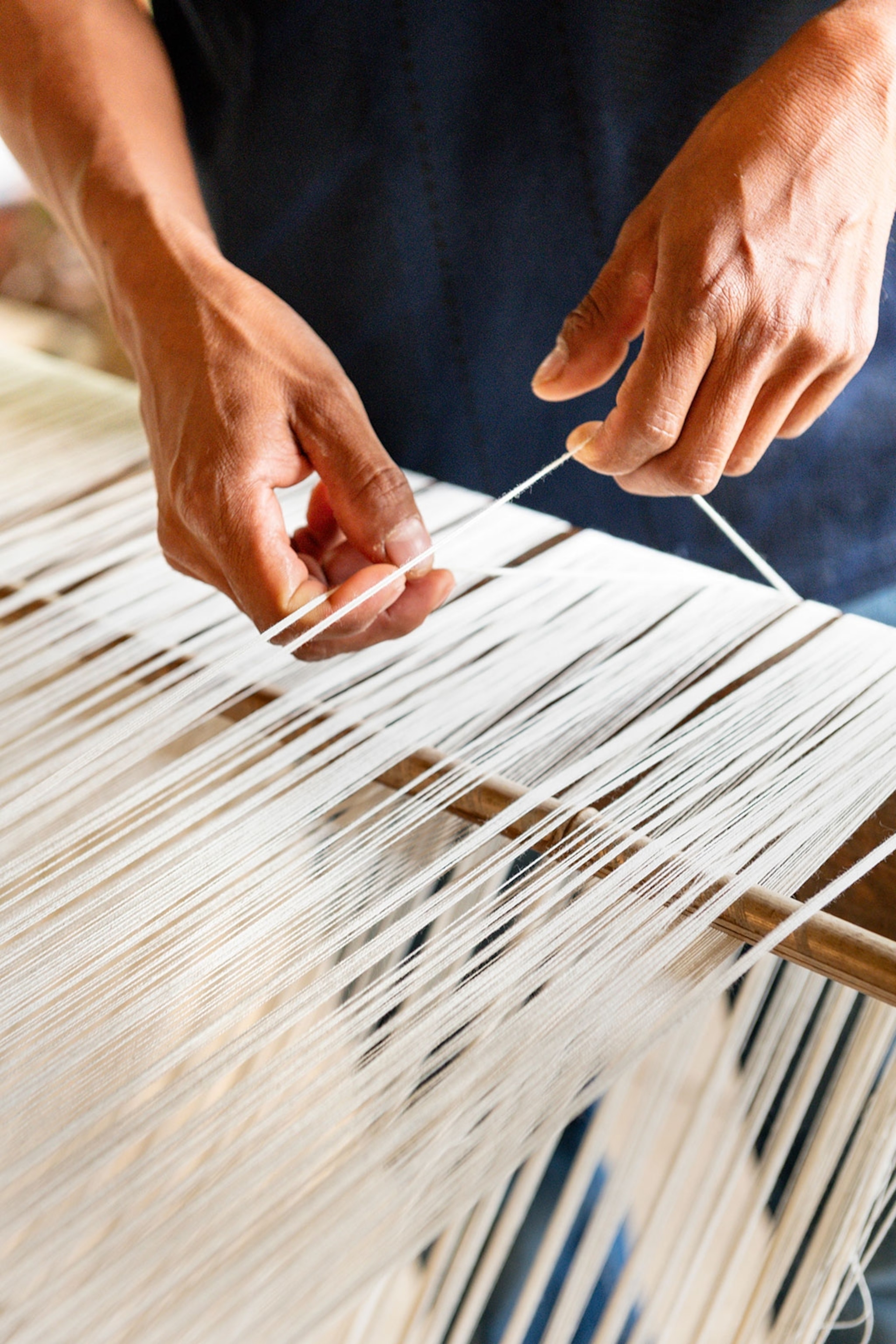 A close-up of hands weaving threads on a machine in El Salvador.