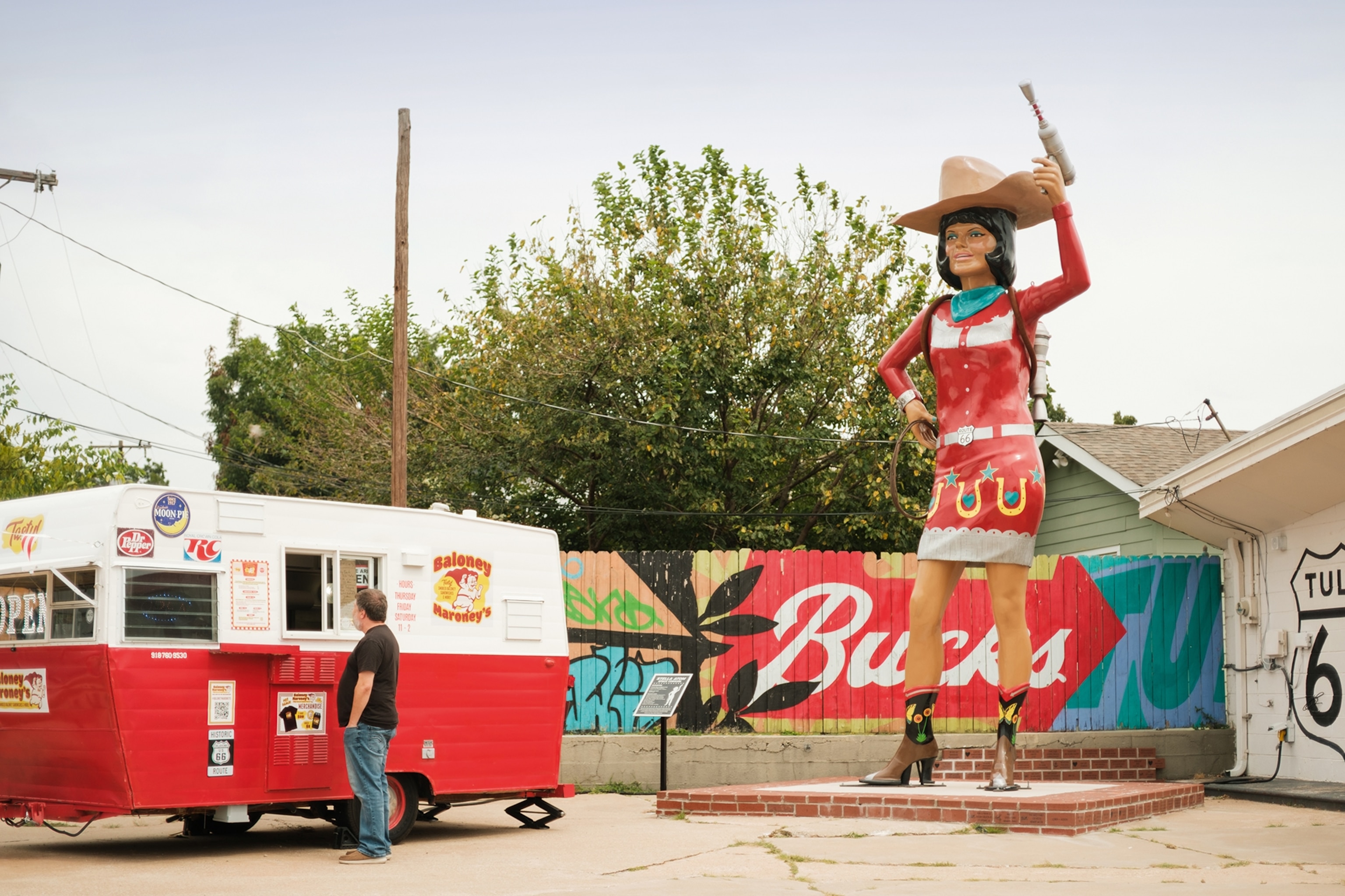 A roadside scene with a giant fibreglass figure of a cowgirl stood next to a food truck.