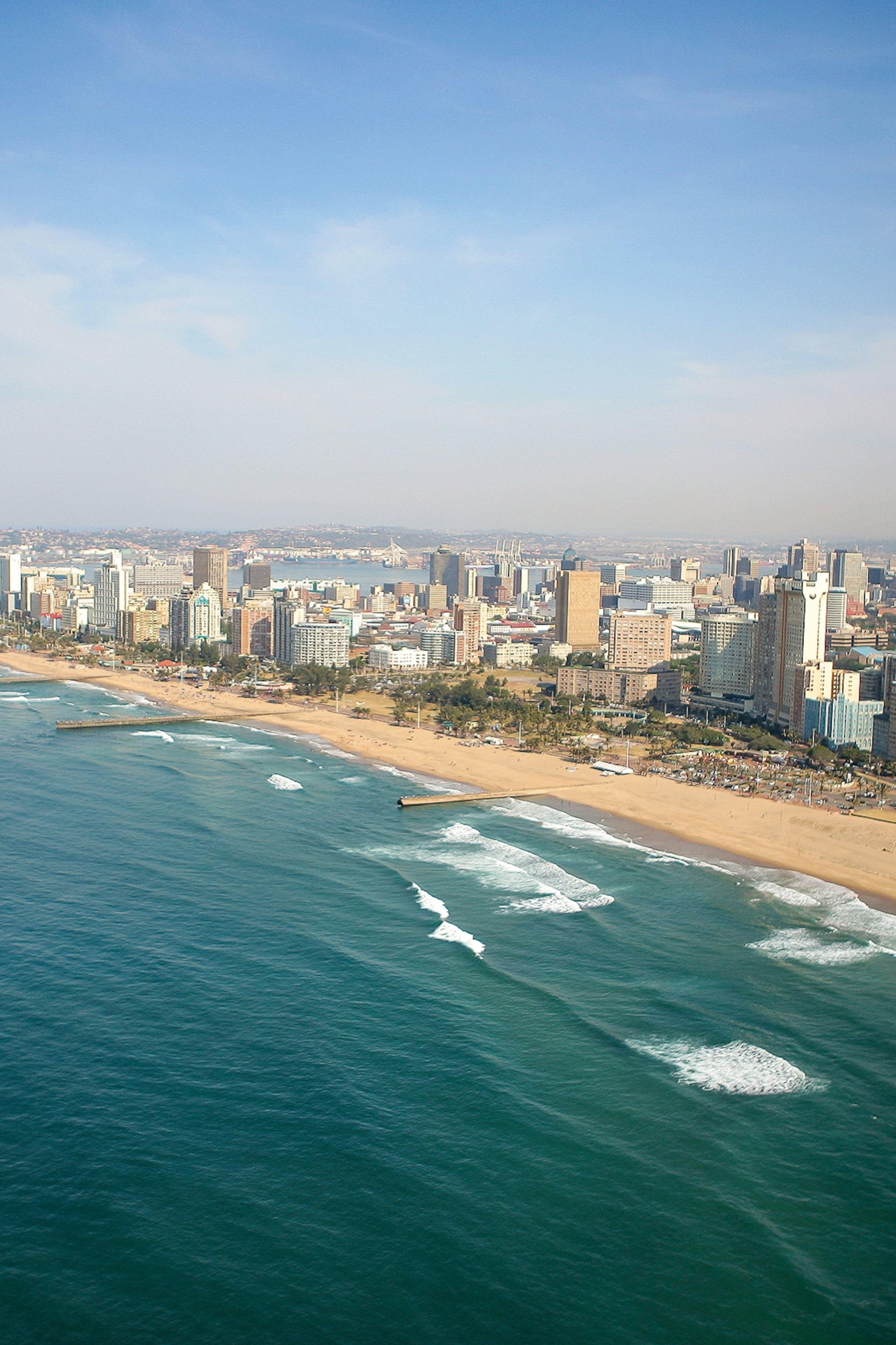 A bird's eye perspective of a coastal city with a beach serving as the only border to skyscrapers rising into the clouds.