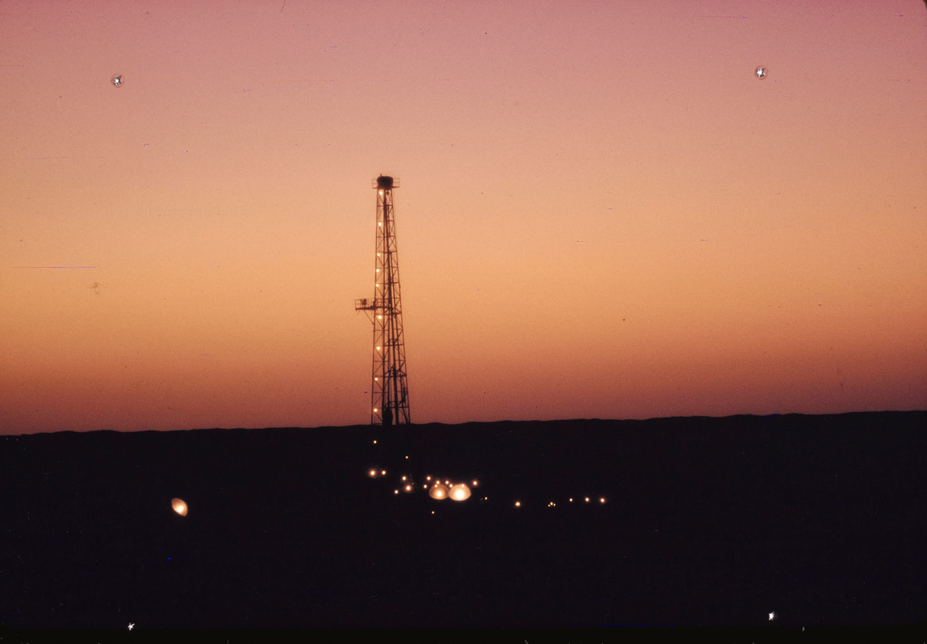 An oil derrick looms like an aviation beacon above the desert at a drilling camp.