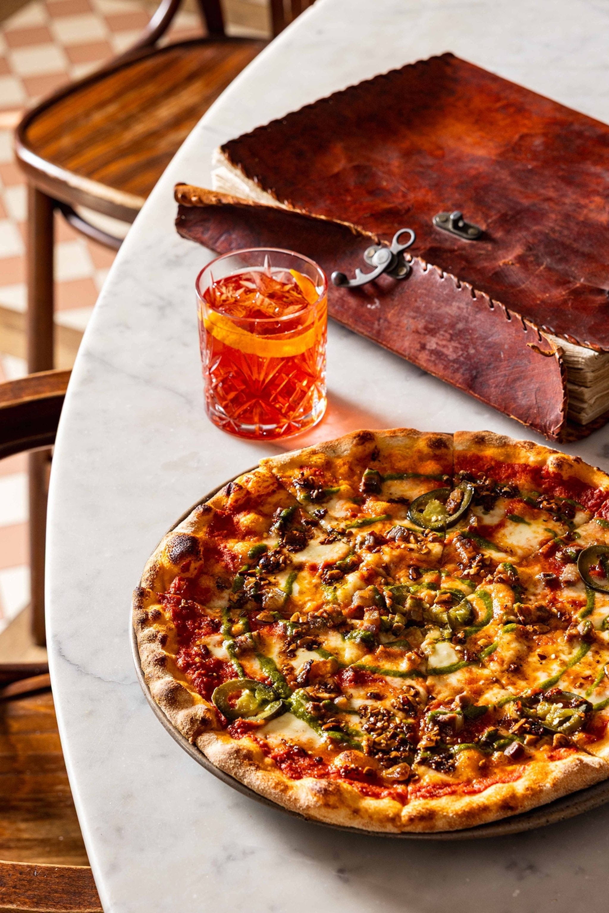 A pizza with various toppings served on a plate with a negroni on the side.