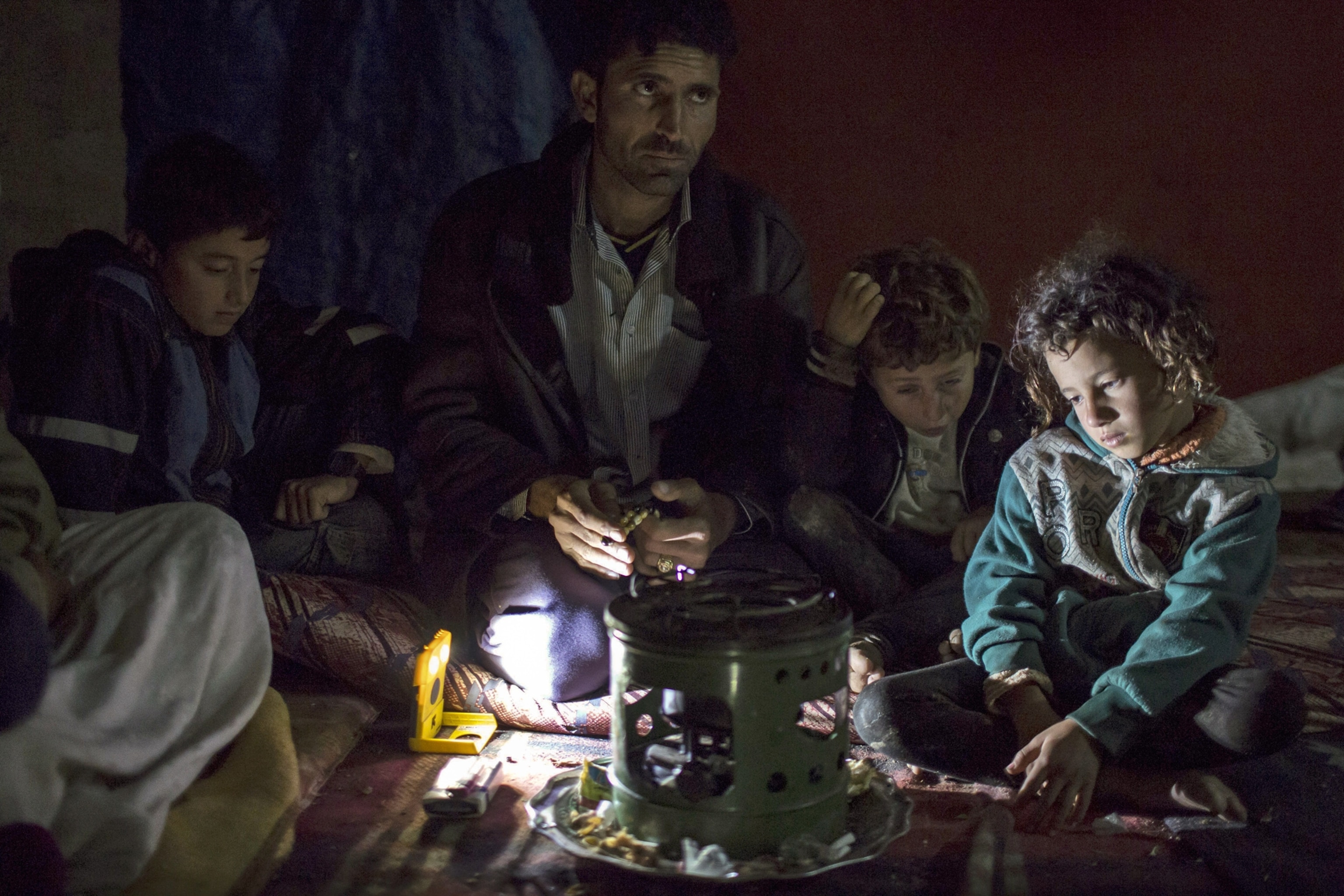 a refugee wrapping himself with a blanket as he stands on a muddy path during wintry weather.