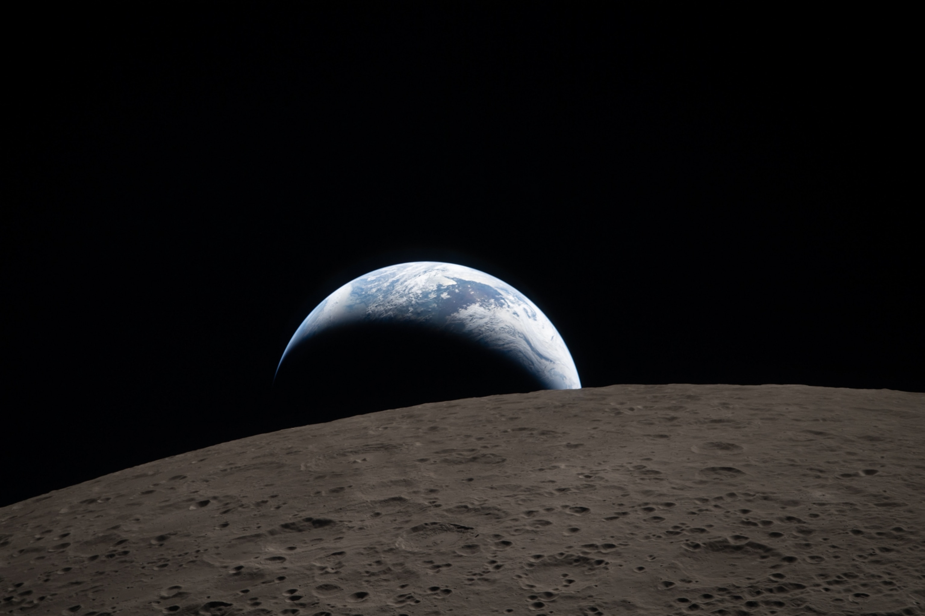 Earthrise over the Moon's horizon, showcasing Earth's blue and white half emerging from the dark space above the Moon's gray, cratered surface.