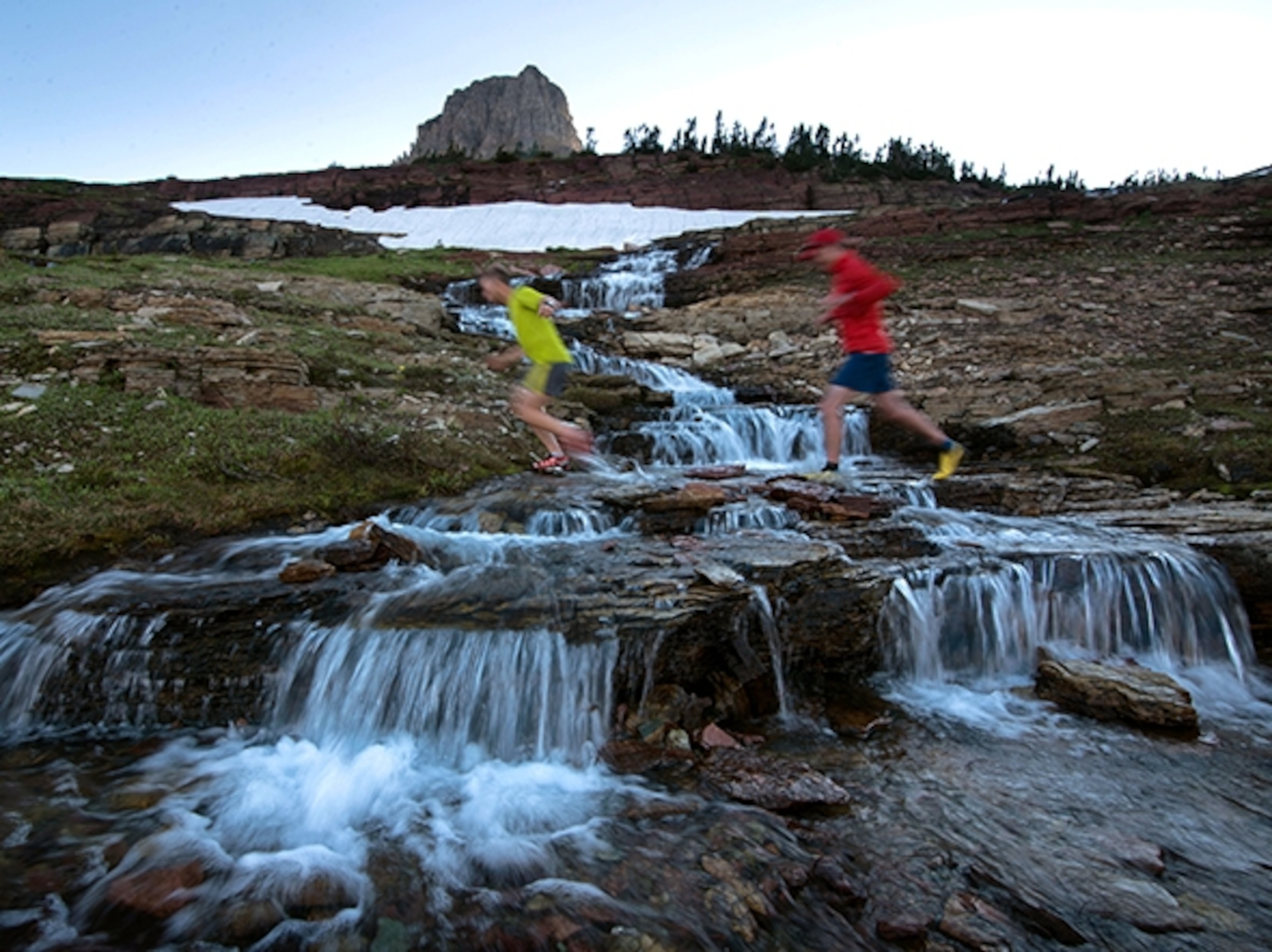 Brody Leven and Joe Johnson run across a glacial runoff creek in Glacier National Park; Photograph by Max Lowe