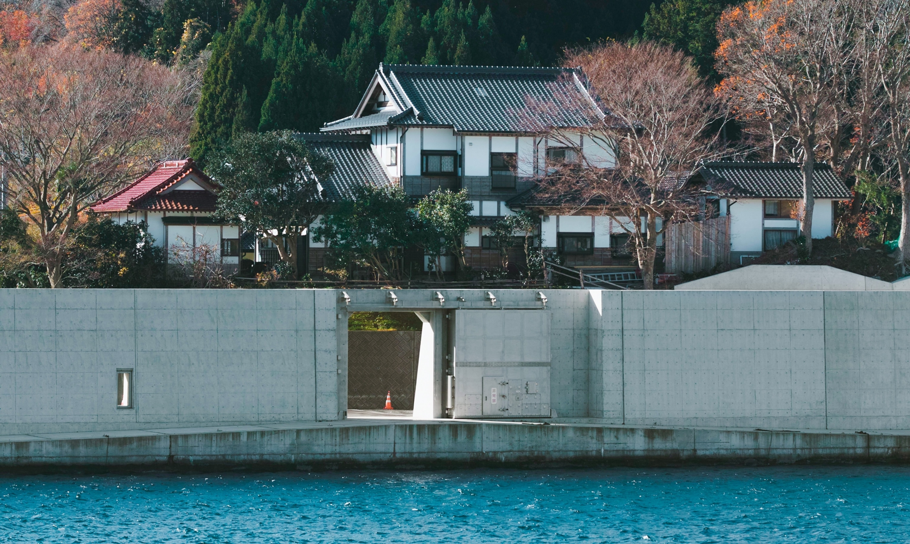 Waterfront houses behind concrete wall with open gate.