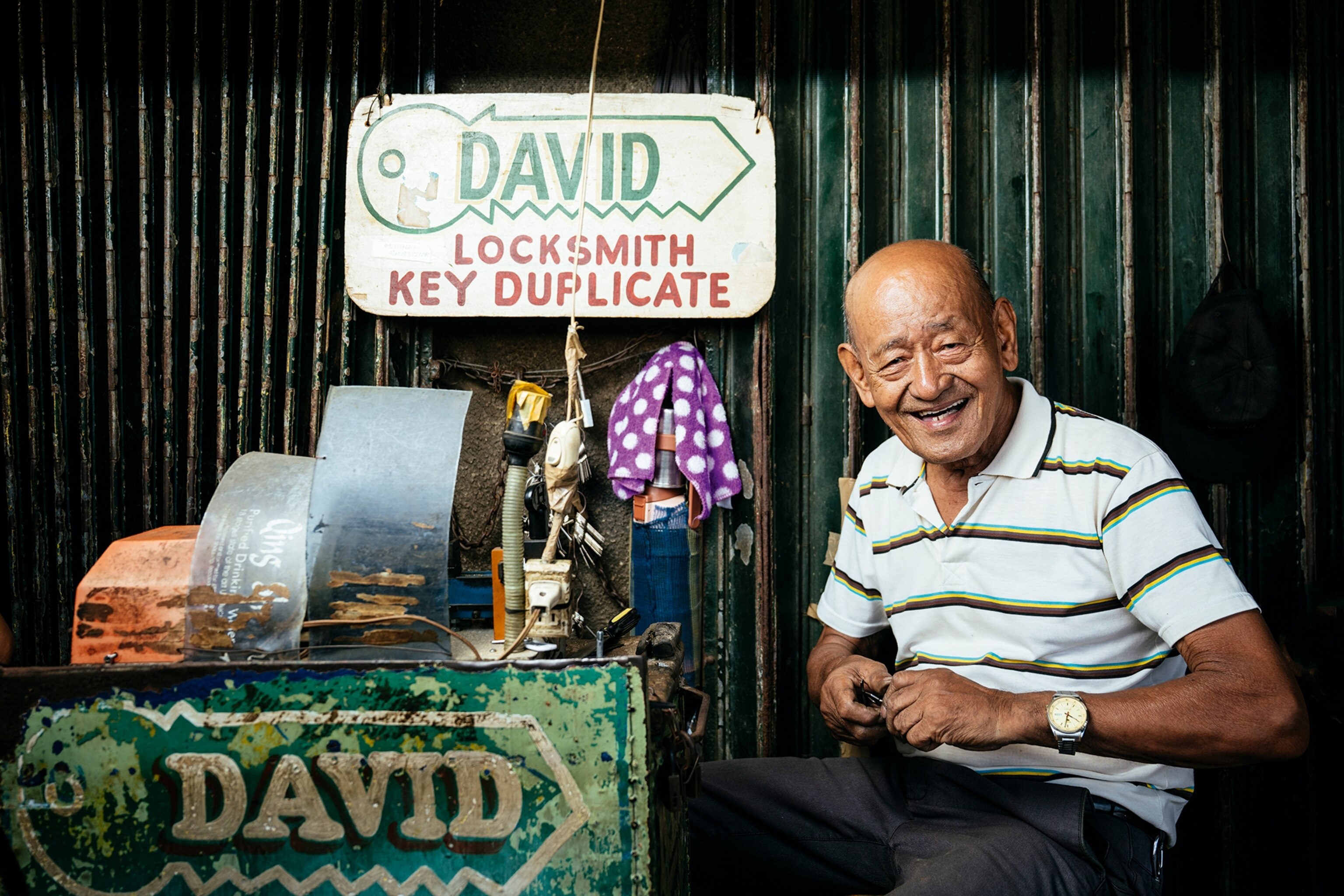 An elderly street seller next to his stall and laughing brightly.