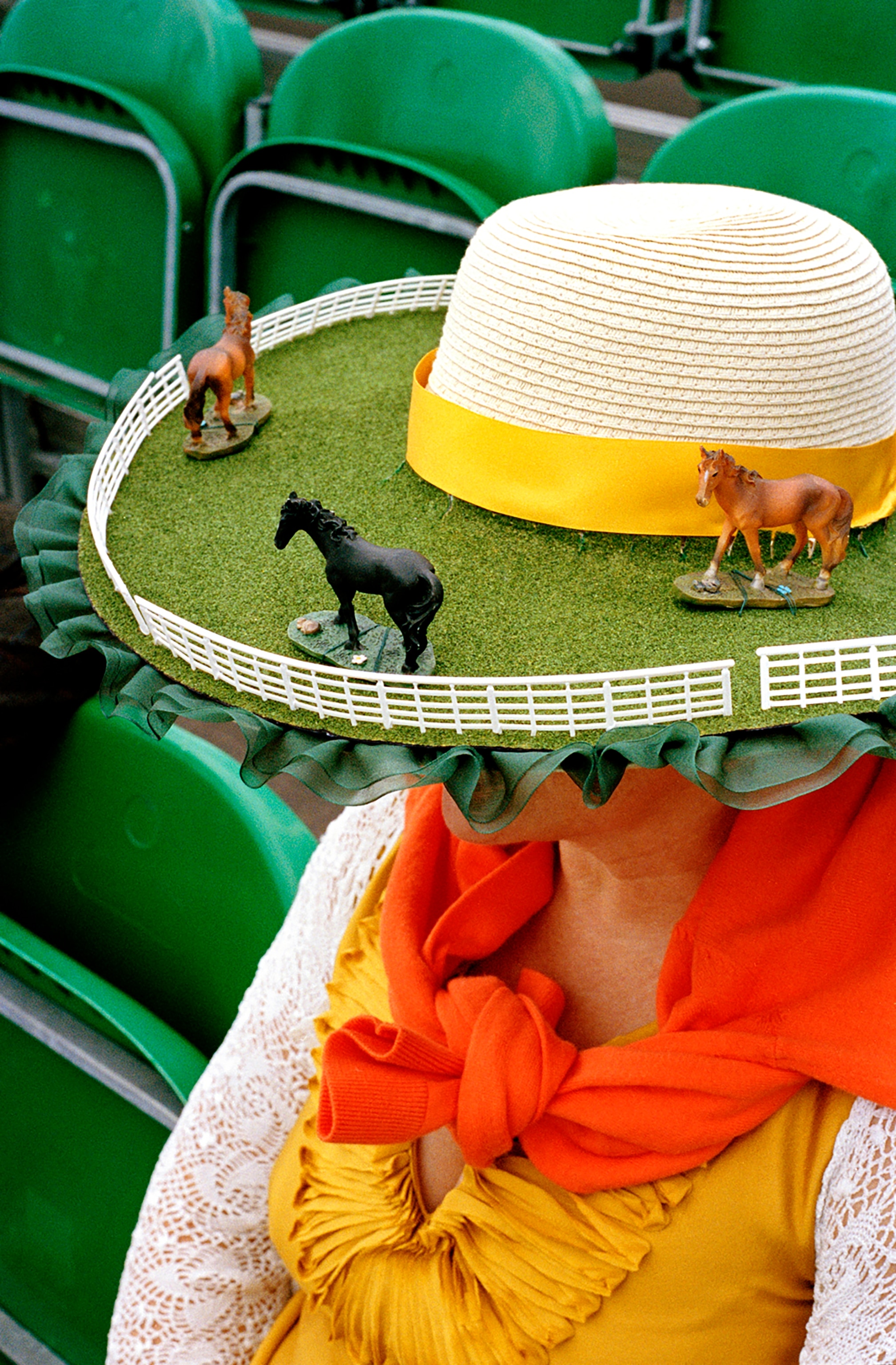 A rimmed hat with plastic horses and fences glue to it, blocking the face of the person wearing it.