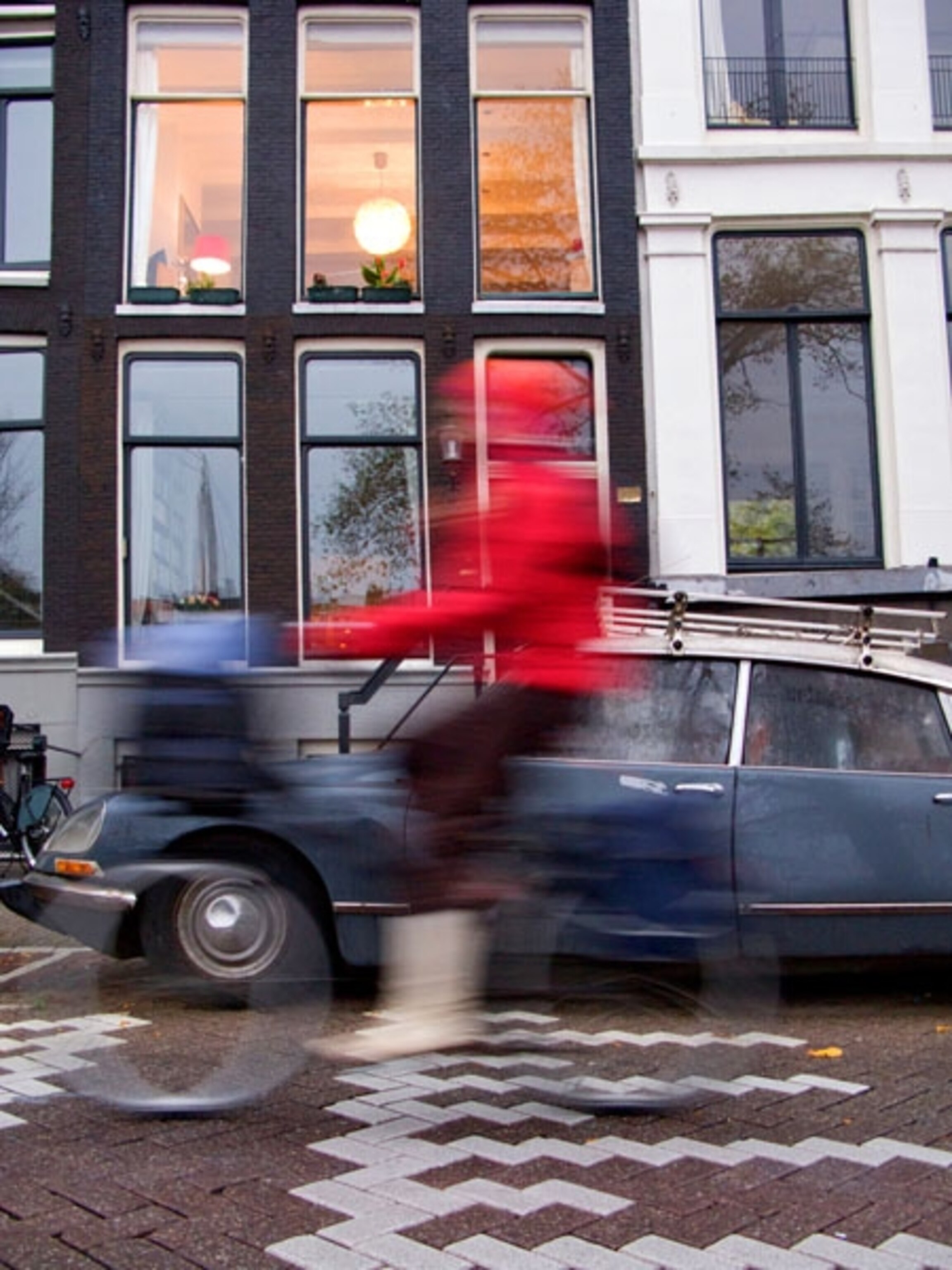 A person in a red jacket rides a bike on the street in Amsterdam