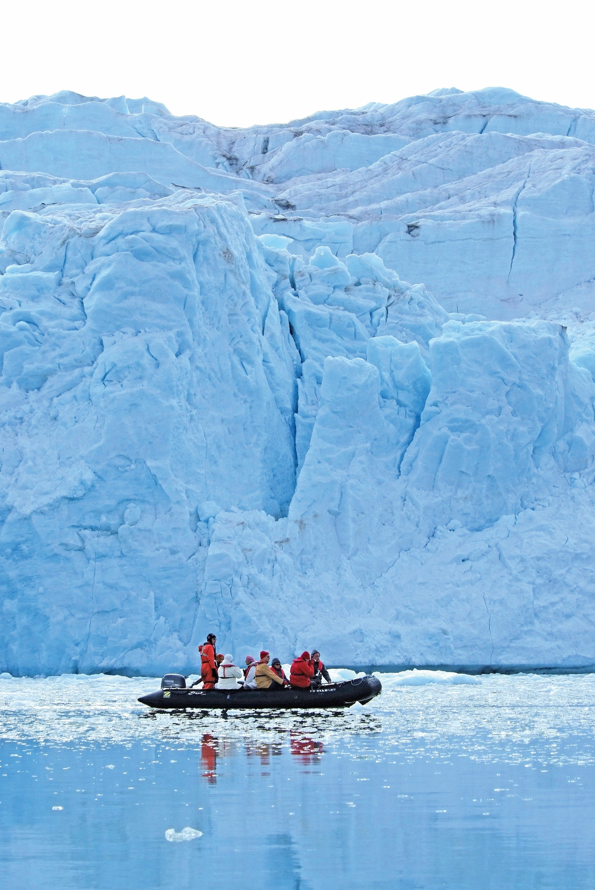 A group explores the glaciers of Svalbard in a Zodiac, a rigid inflatable boat. The water is glassy and still.