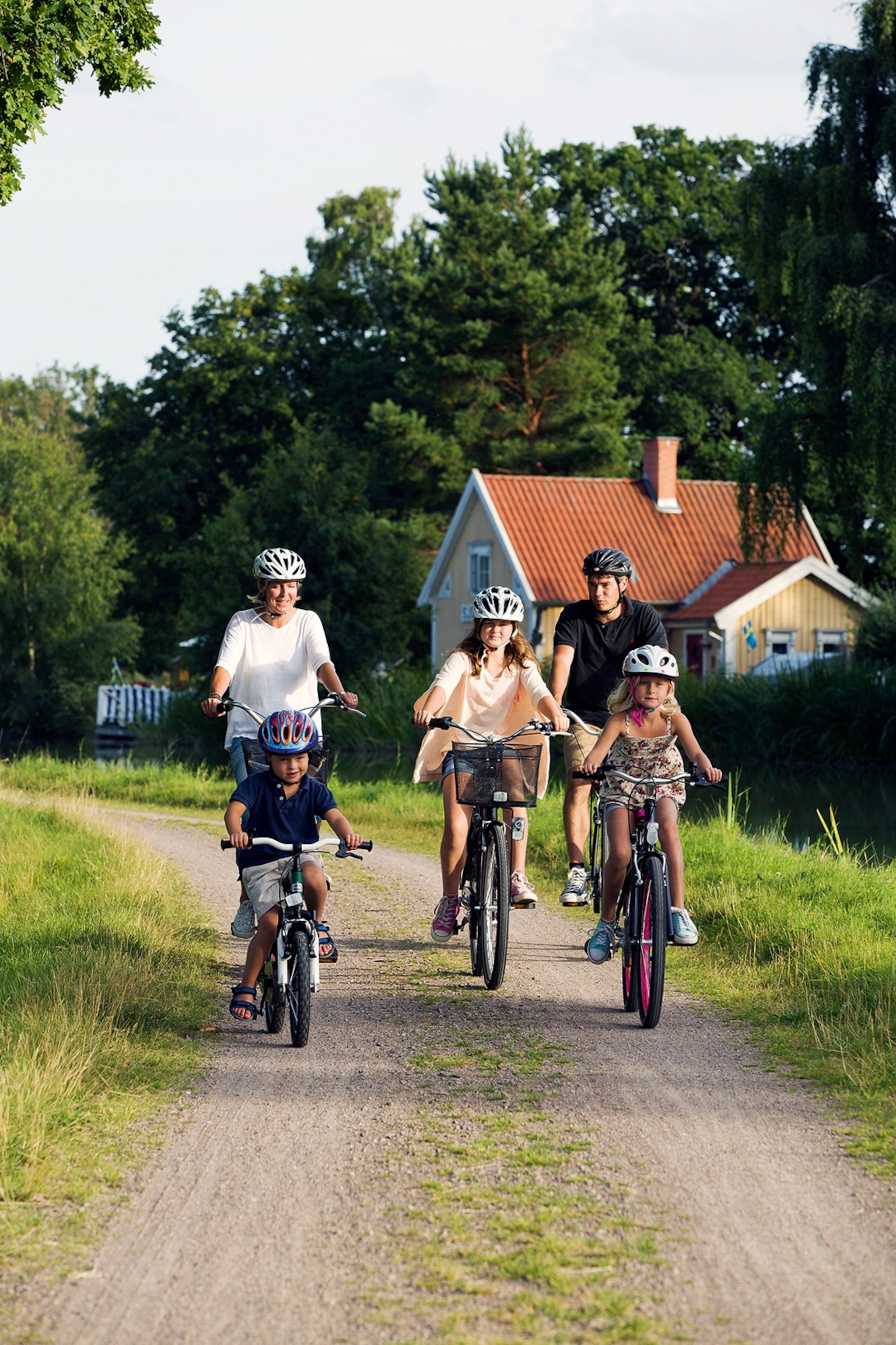 A four-piece family cycling along a path leading past houses in a forest.