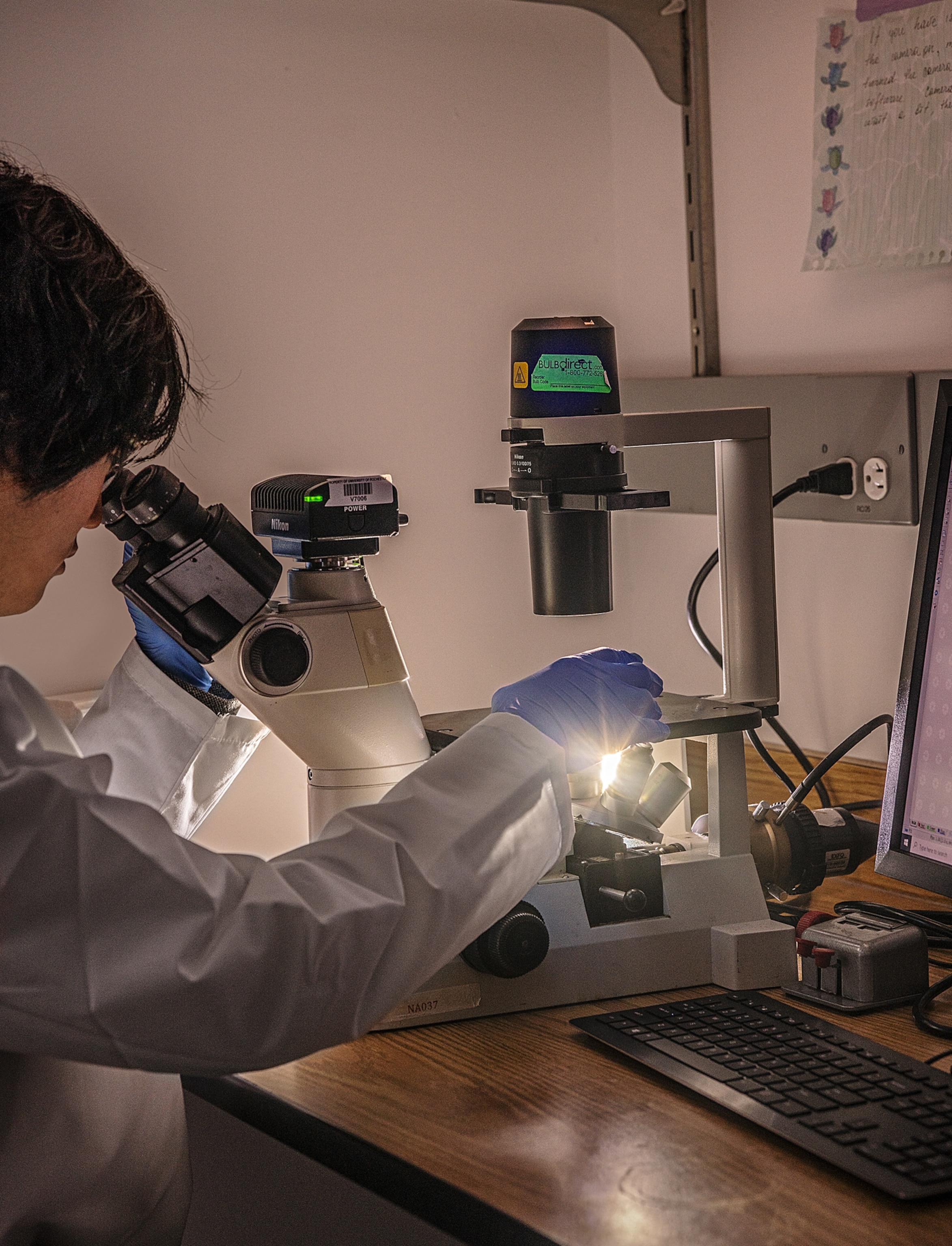 In dark room woman looking into microscope.
