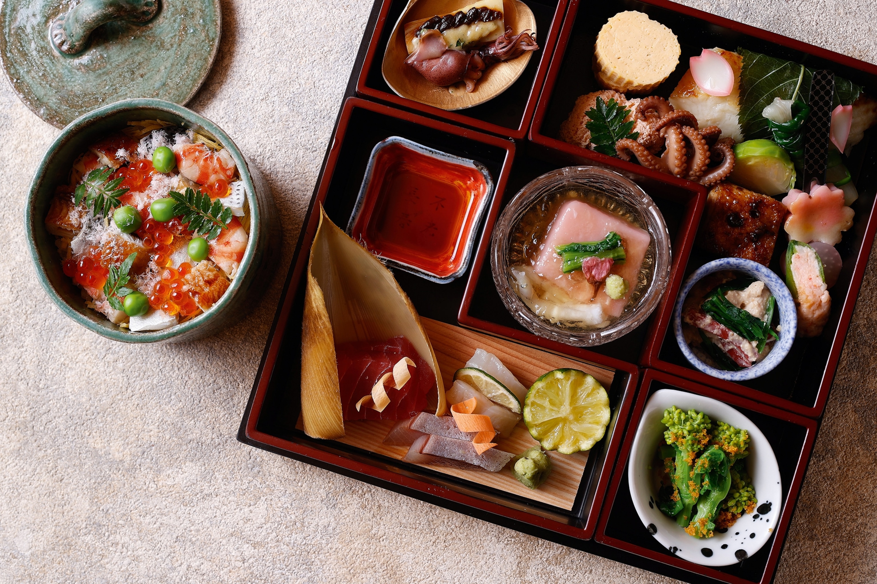A birds-eye view of a enamel bento box with multiple compartments, each containing an artfully arranged bite of fish or seafood.