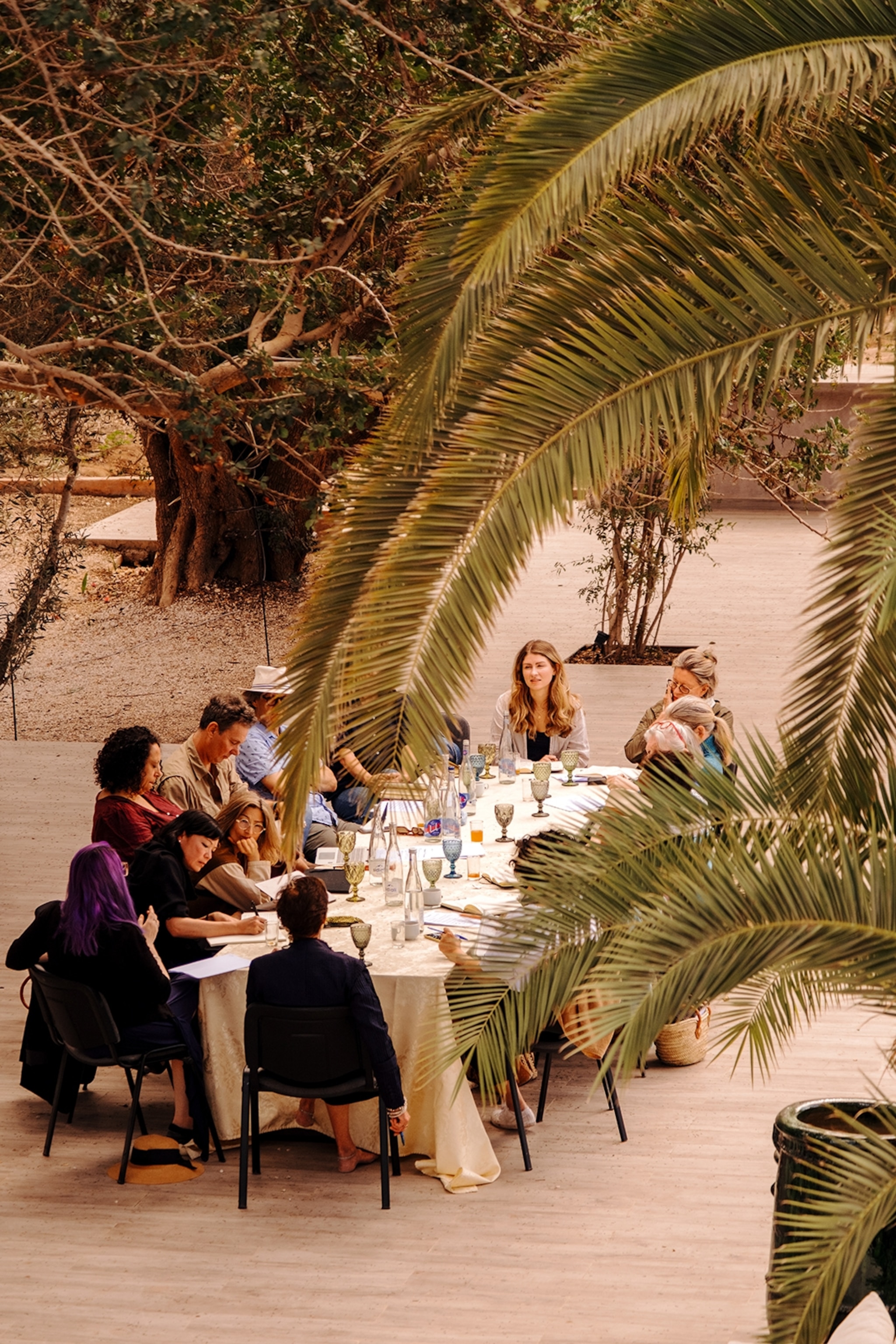 An outdoor dinner table on a terrace, shot through palm trees, with a group of writers.