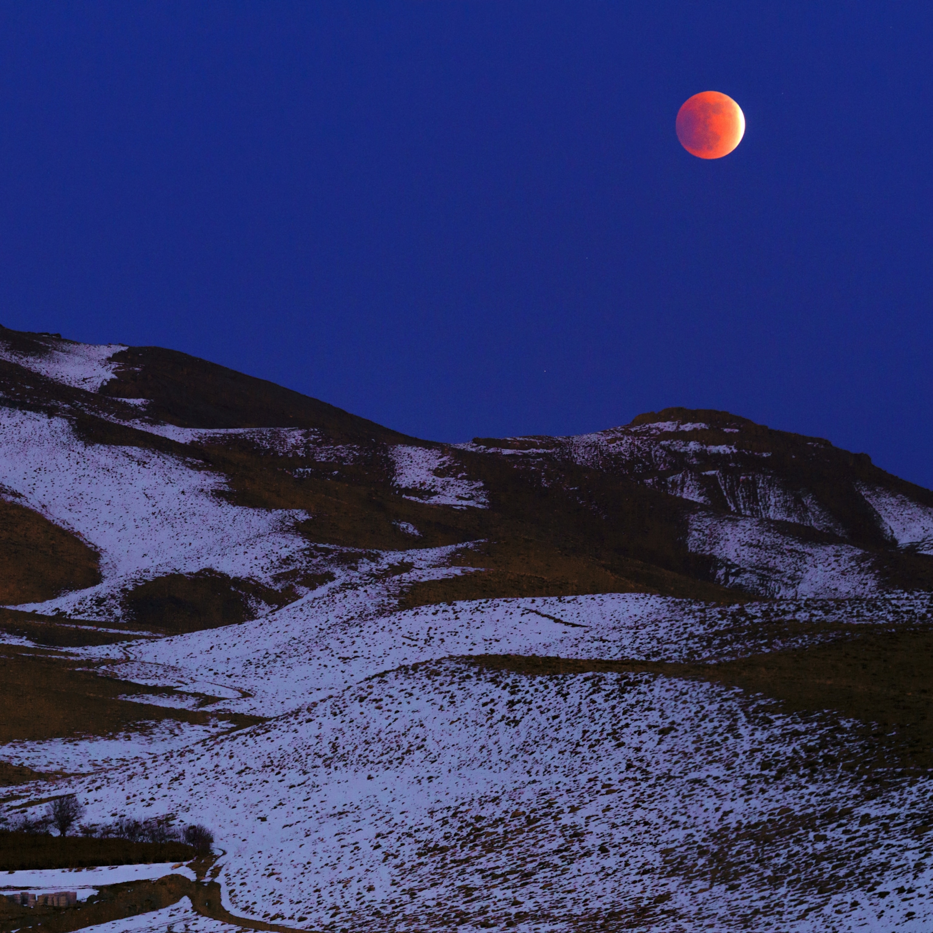 The total lunar eclipse of December 2011 in the evening twilight over the snowy Zagros Mountains. Kashan, Zagros Mountains, Isfahan, Iran.