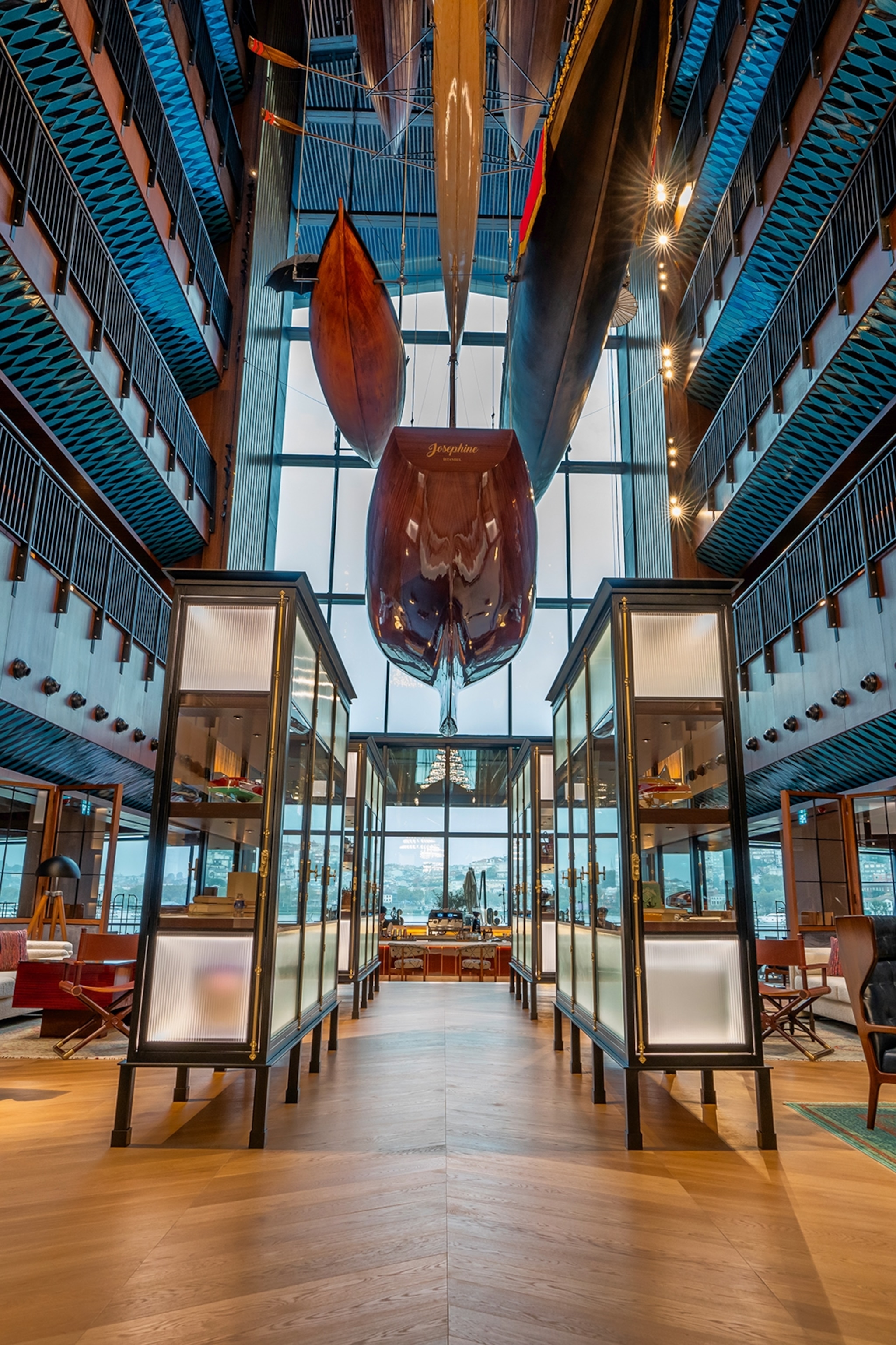 The tall interiors of a modern hotel lobby with boats hung in between the balconied hotel floors.