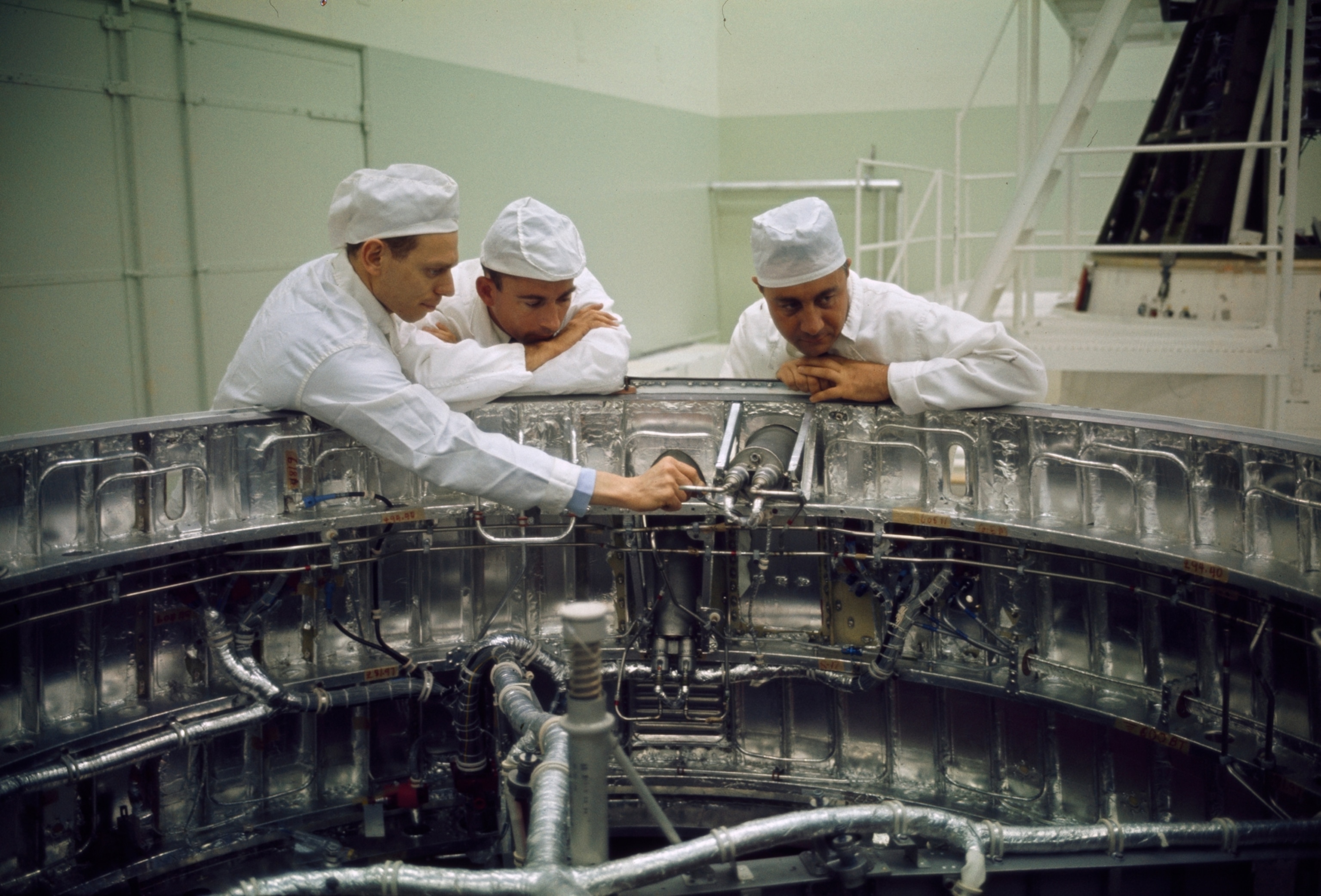 Men inspect spacecraft adapter rings in a dust-filtering clean room.