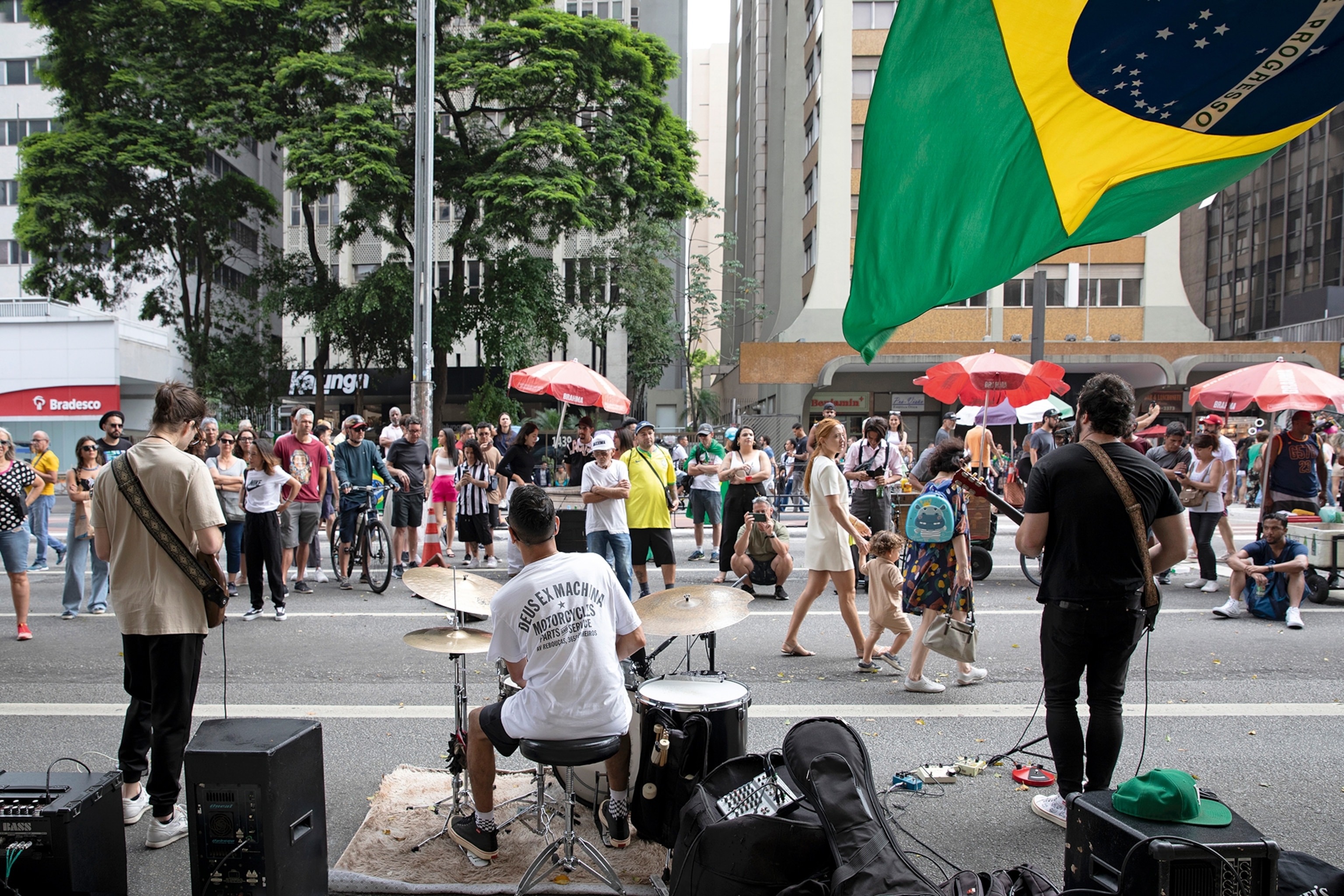 A street party in Sao Paulo with a band playing music and the Brazilian flag waving in the corner.