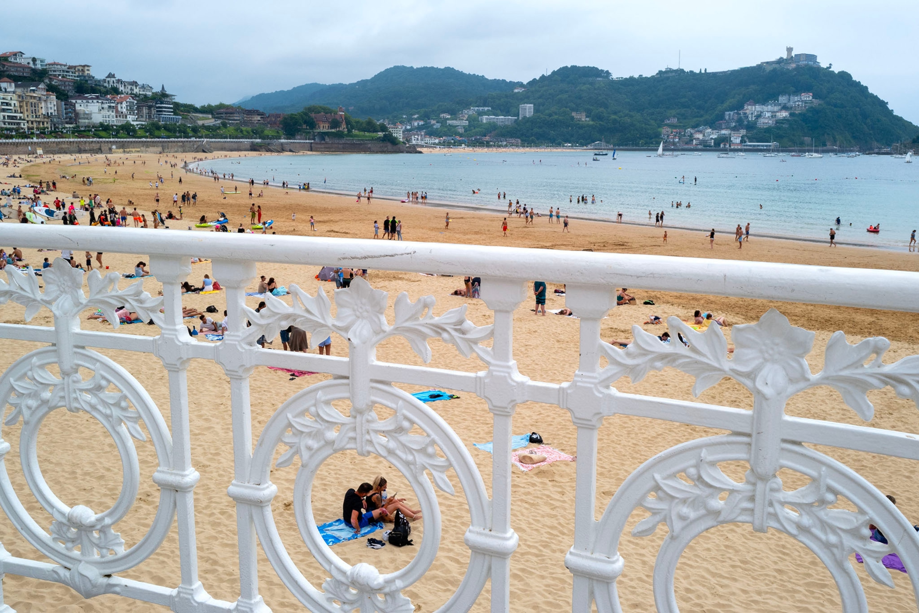 SAN SEBASTIAN, SPAIN - August 6, 2021 Beachgoers relax on La Concha, the centerpiece of San Sebastian's beach scene. The long stretch of sand vanishes at high tide beneath the Bay of Biscay's massive tide changes. La Concha was a glamorous destination in the 19th century and appears in Ernest Hemingway's "The Sun Also Rises." It became a health retreat after Queen Isabel II visited and received skin treatments there.