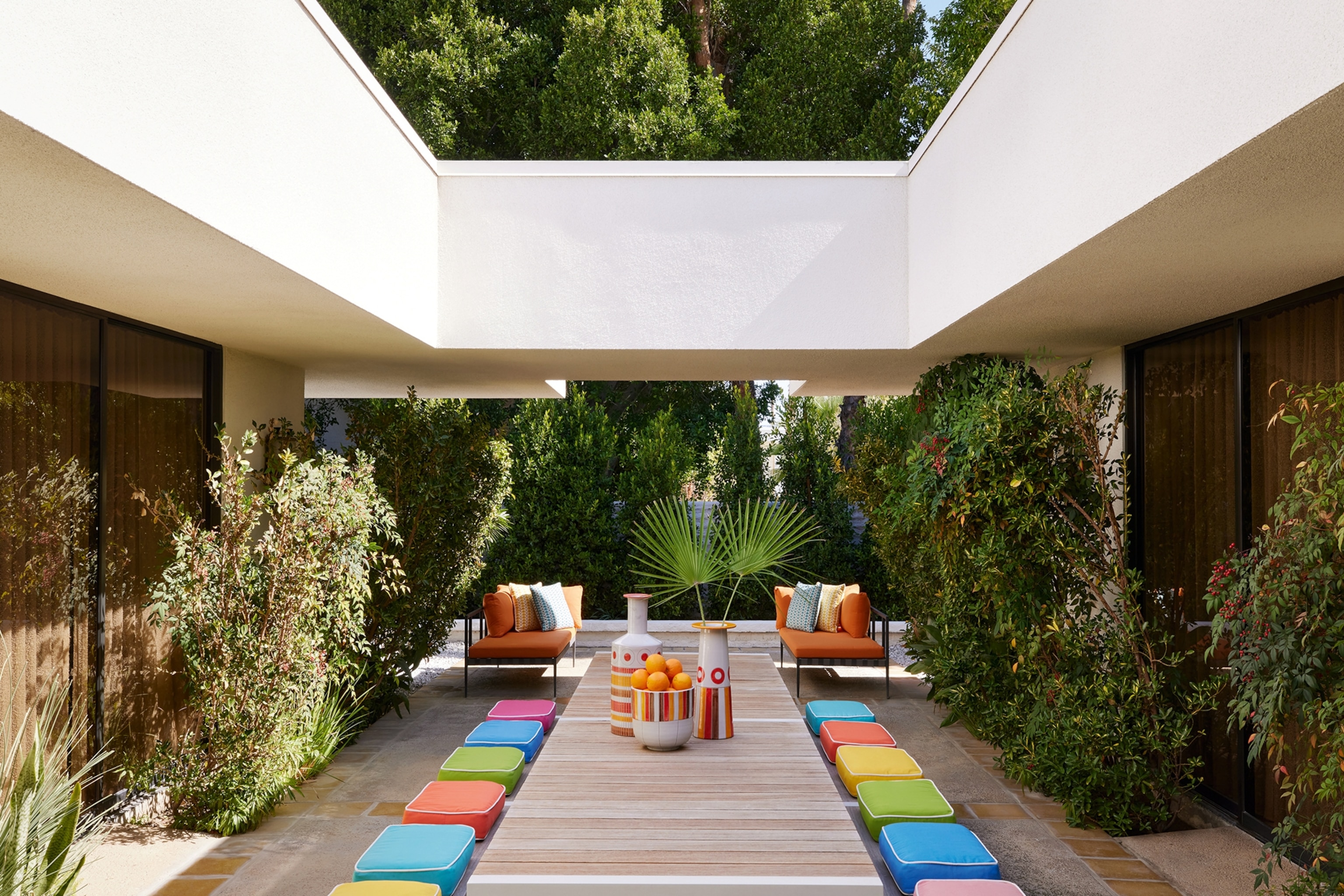 The patio area of a hotel with colourful seat cushions on long benches, framing a table decorated with mid-century modernist ceramics.