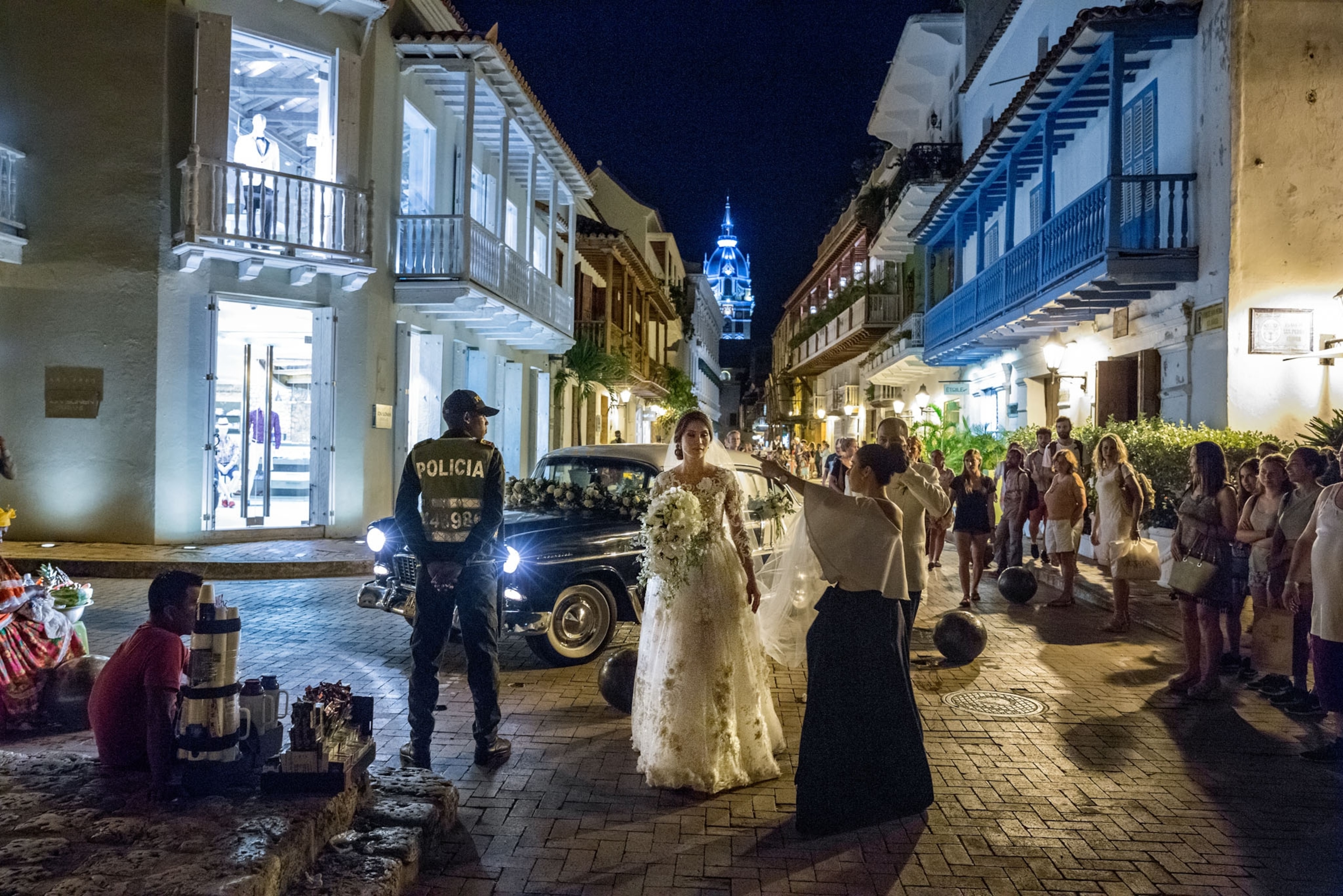 a bride at night on a cobble stone street as pedestrians and police stand by