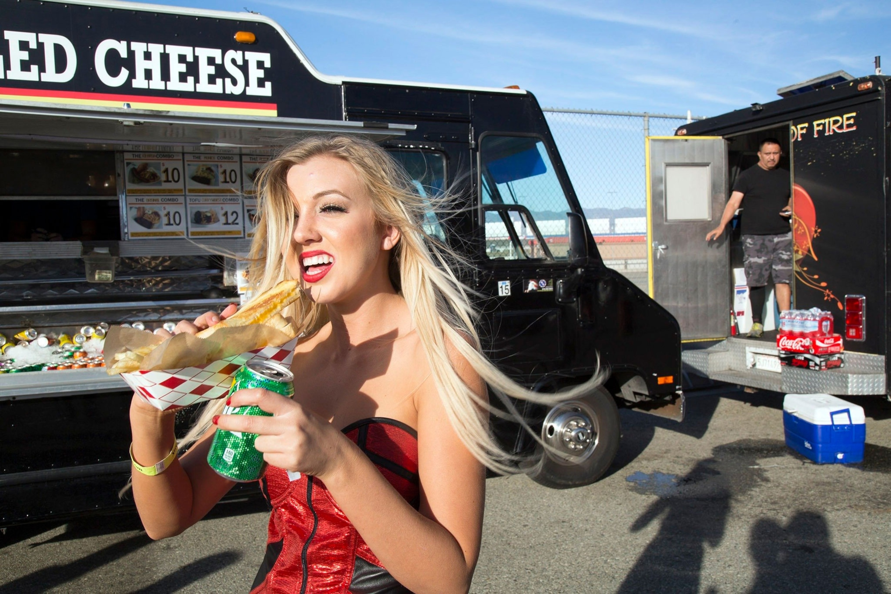 A model eats a grilled cheese sandwich from a food truck at a car show